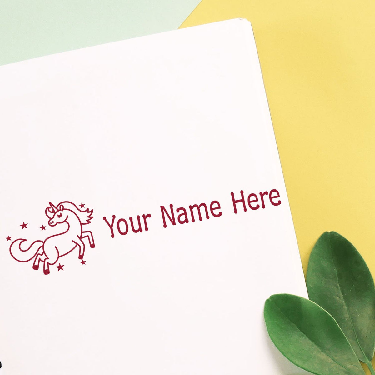 Custom burgundy unicorn stamp and seal on white paper with Your Name Here, yellow background and green leaves.