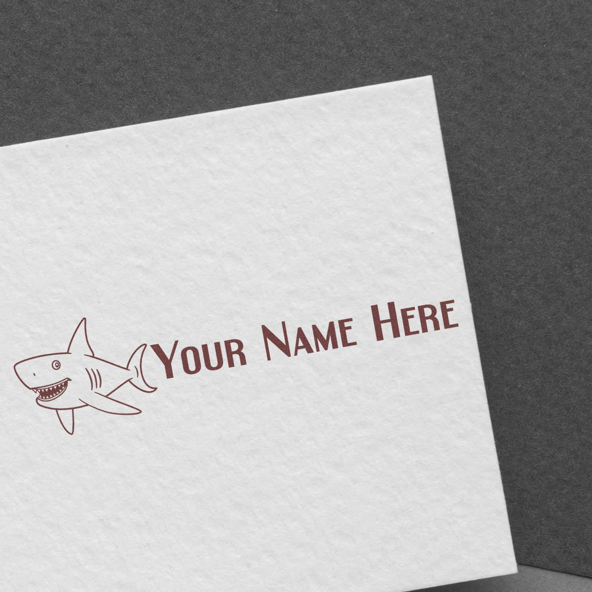Custom brown shark stamp seal with Your Name Here on white paper, set against a dark gray background.