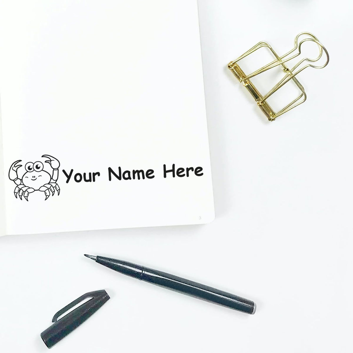 Personalized crab stamp seal with black text, gold binder clip, and black pen on a clean white background.