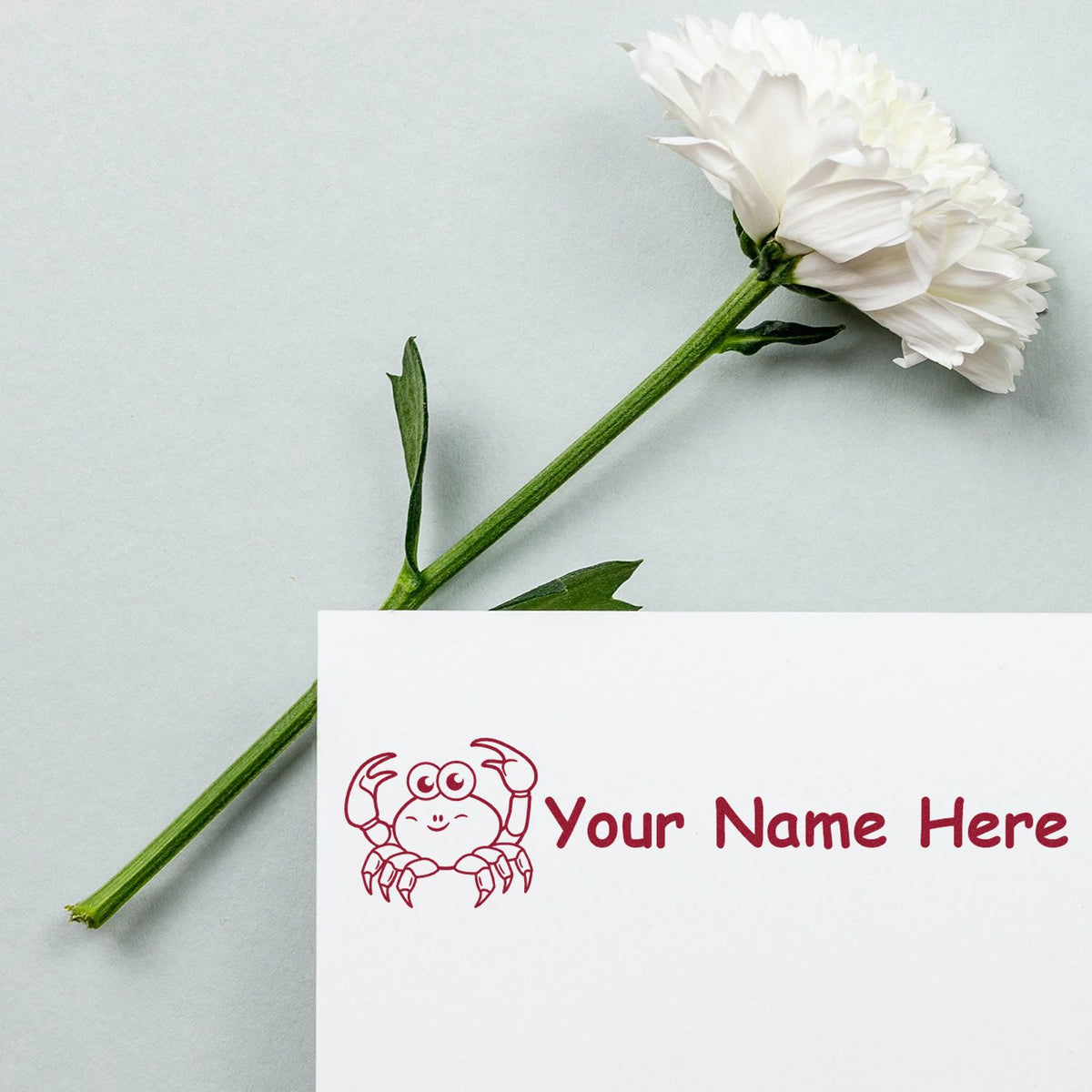 Red crab custom stamp and seal with Your Name Here beside a white flower on a pale background.
