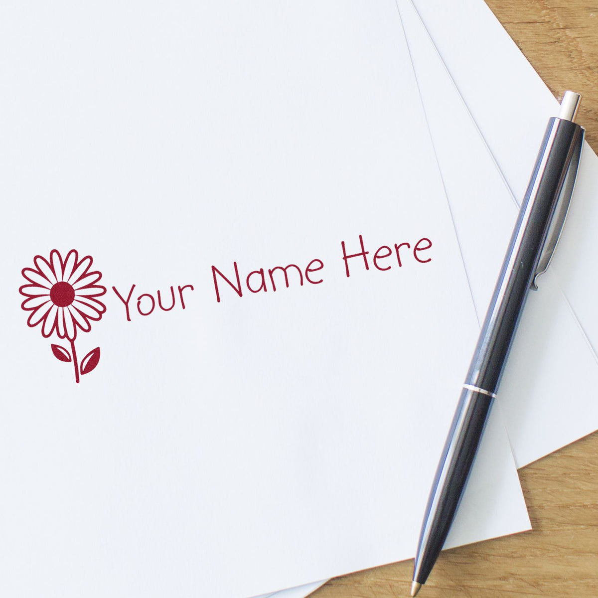 Maroon custom stamp and seal with flower logo and Your Name Here beside a black pen on white paper.