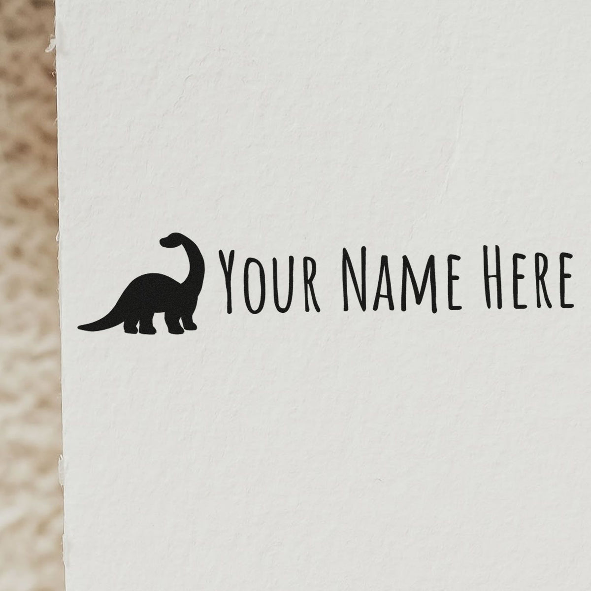 Black dinosaur stamp with Your Name Here text on white paper, a customizable seal product.
