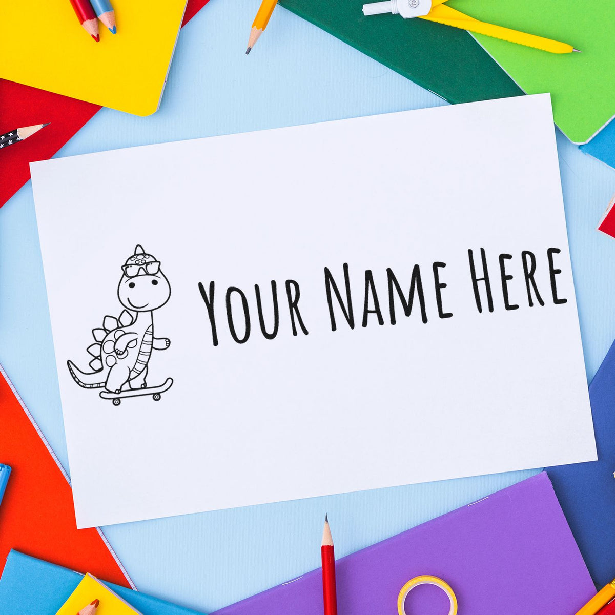 Custom stamp and seal card with a dinosaur on skateboard and Your Name Here, on white paper with colorful pencils and notebooks.