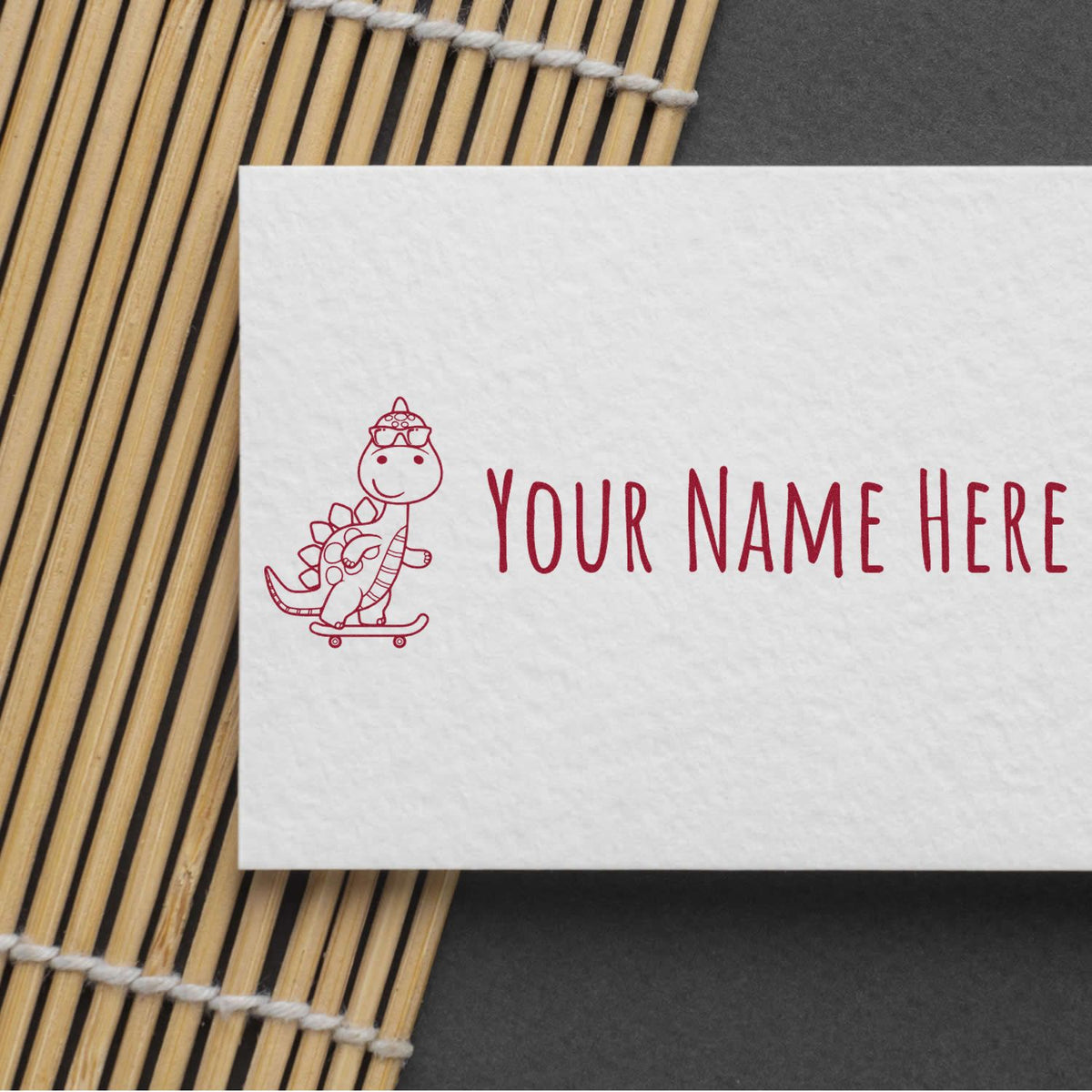 Custom red stamp seal on white card with cartoon dinosaur on skateboard and Your Name Here beside bamboo mat.