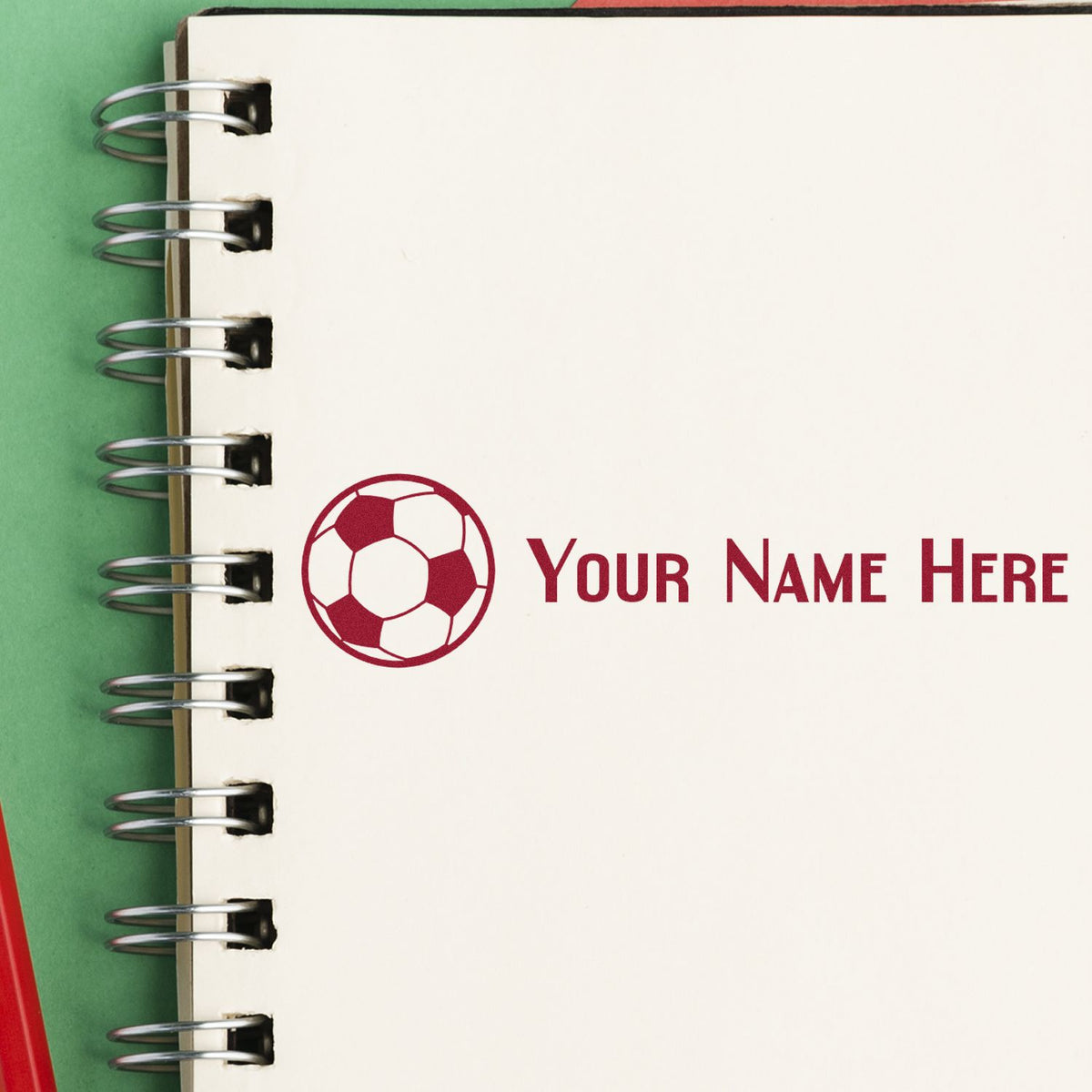 White spiral notebook with red soccer ball stamp and Your Name Here seal on green background