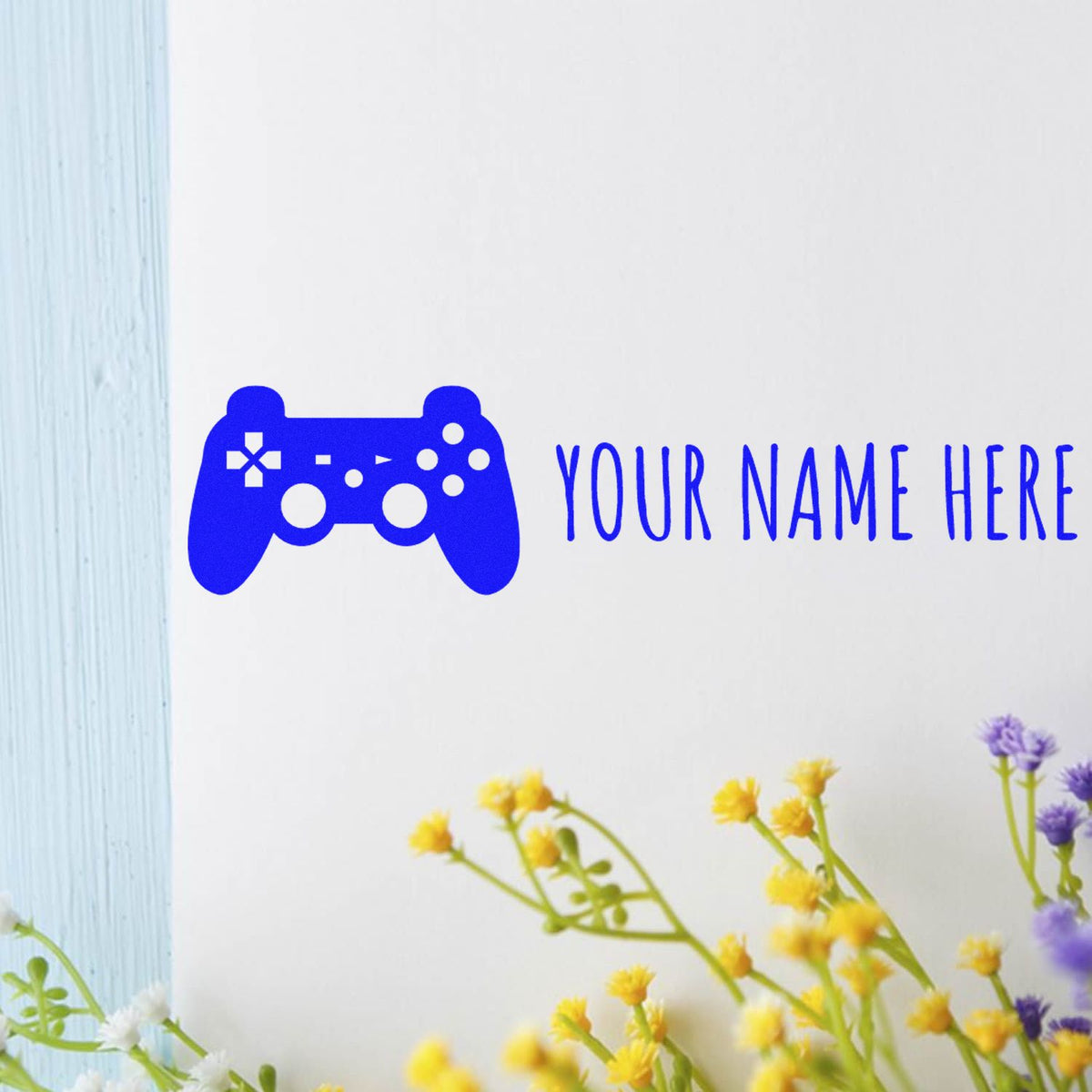 Blue custom stamp and seal with game controller icon and YOUR NAME HERE text on white, with yellow and purple flowers.