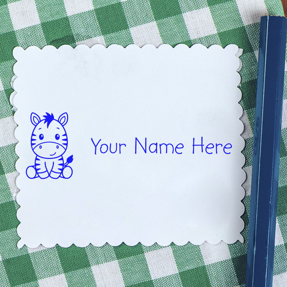 White scalloped name seal stamp with blue zebra and Your Name Here on green gingham background.