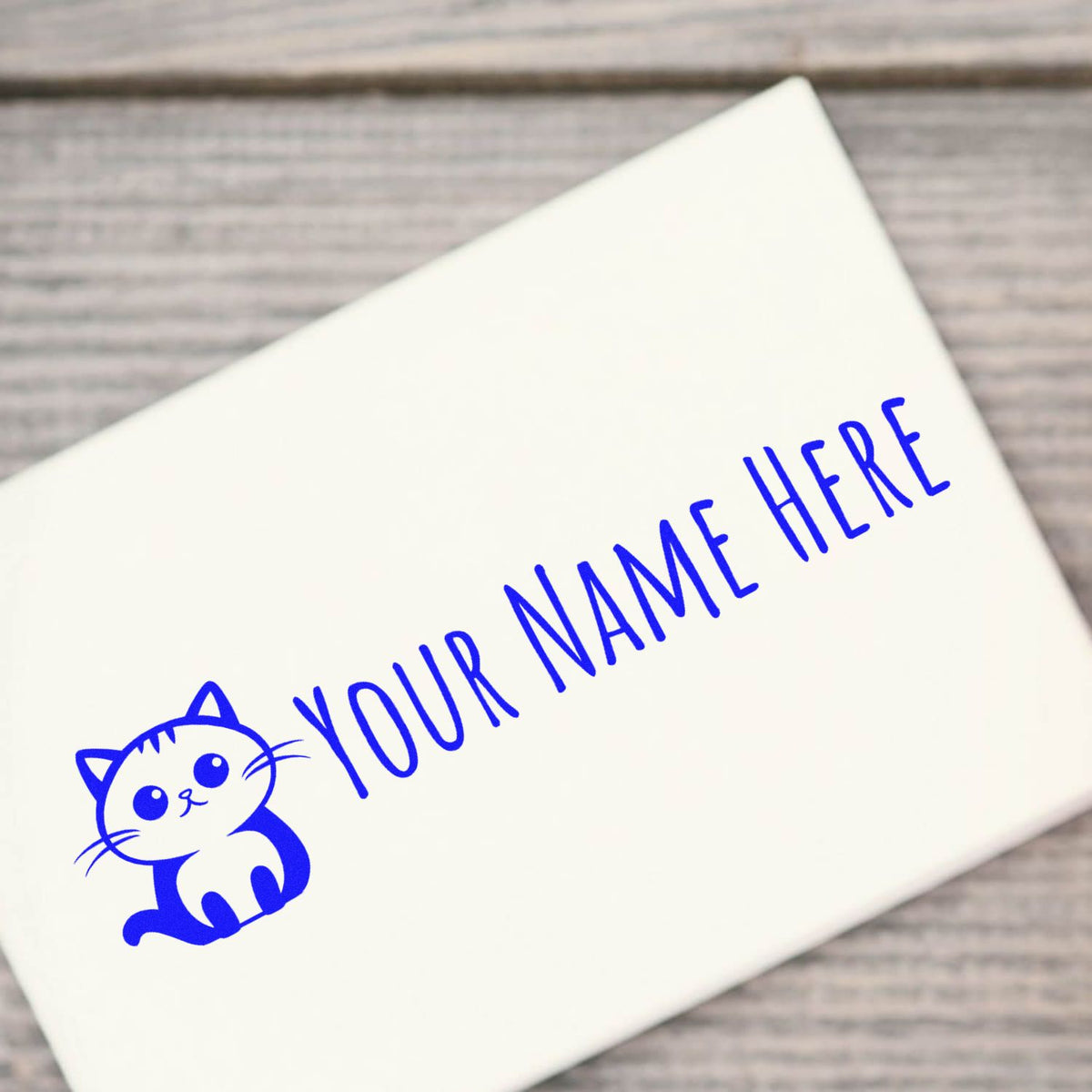 Blue custom name stamp and seal with cat graphic on a white envelope over a wood background.