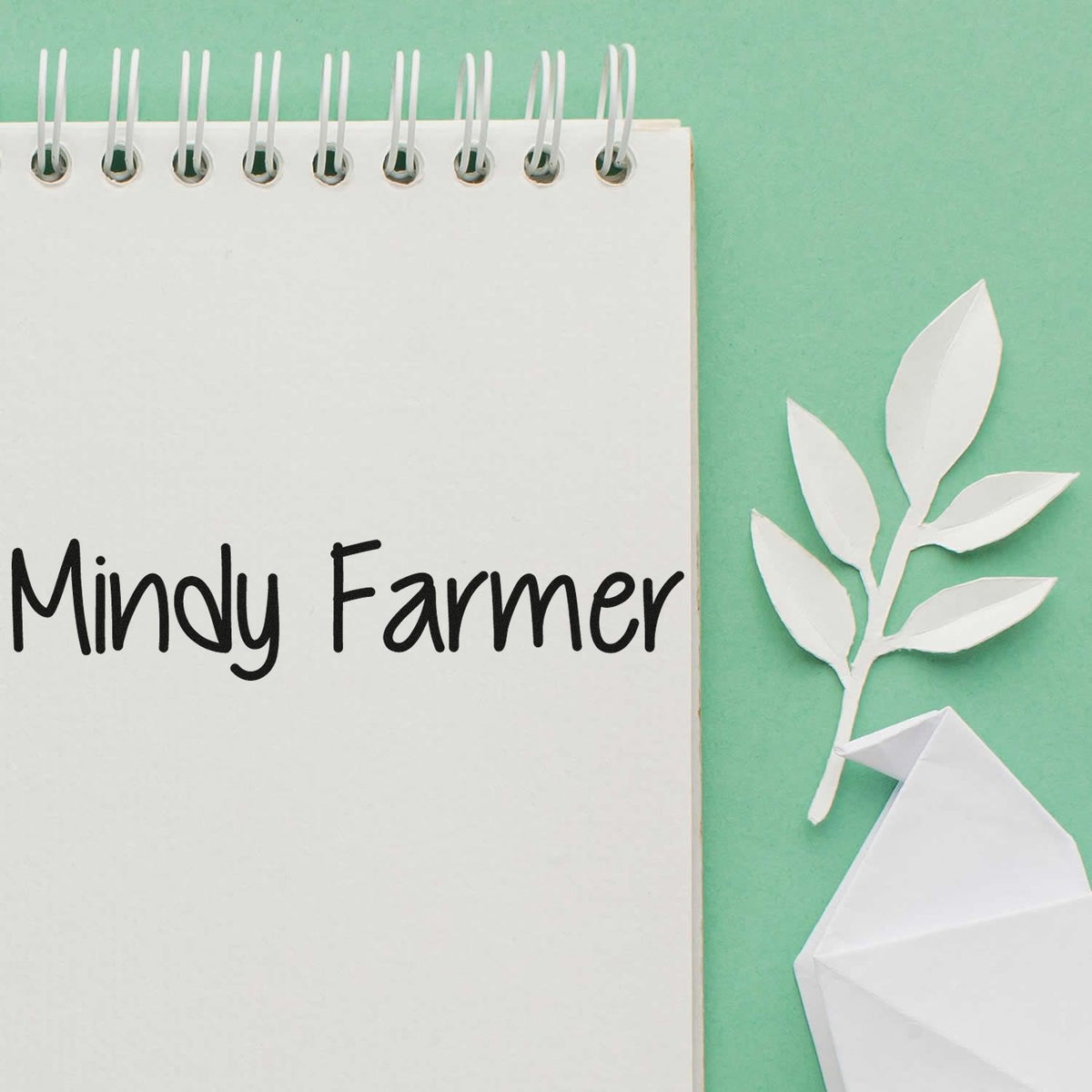 Mindy Farmer custom stamp and seal in black on white spiral notebook, with paper leaves on mint green background.