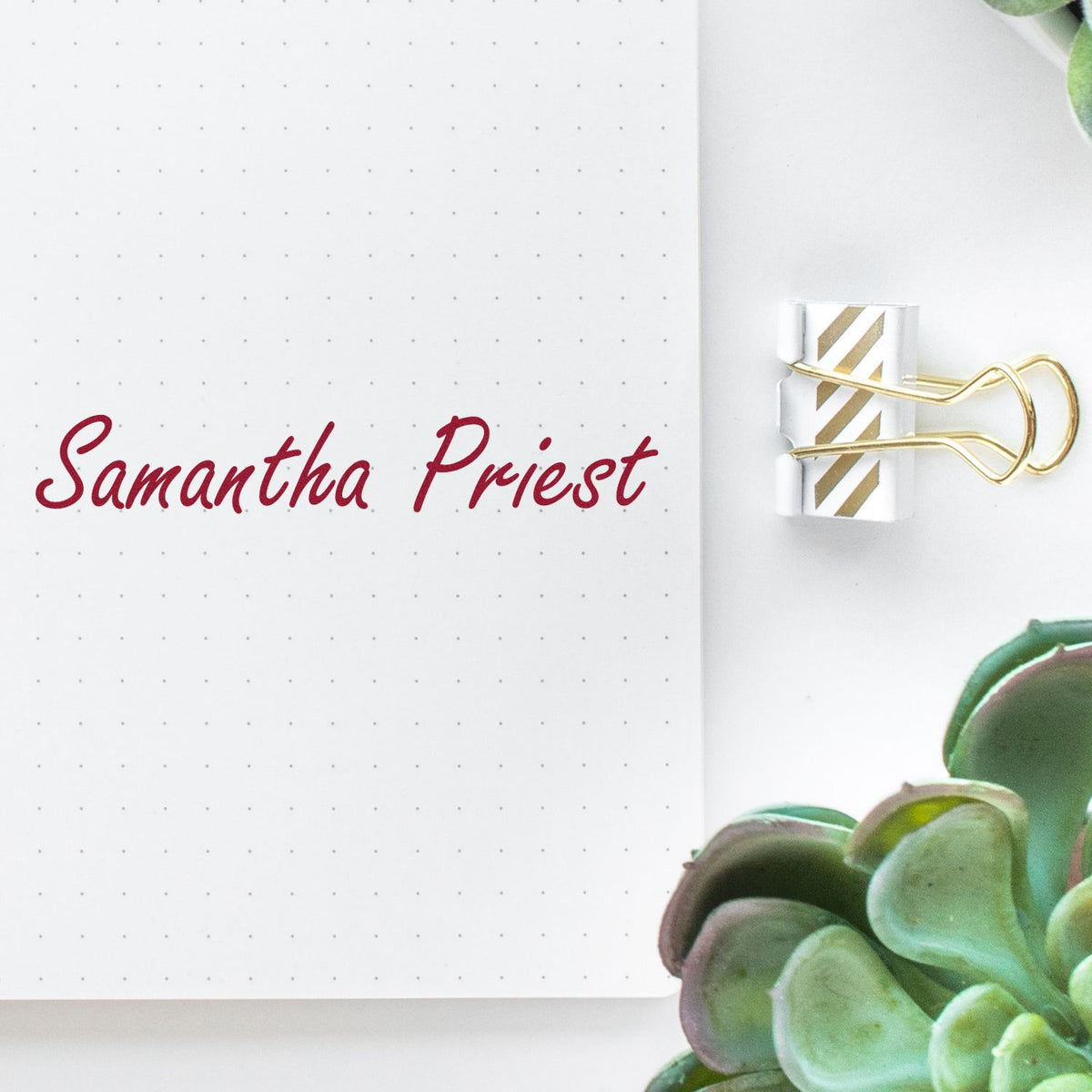 White dotted notebook page with burgundy Samantha Priest script and a gold-striped custom stamp seal clipped with a gold binder clip.