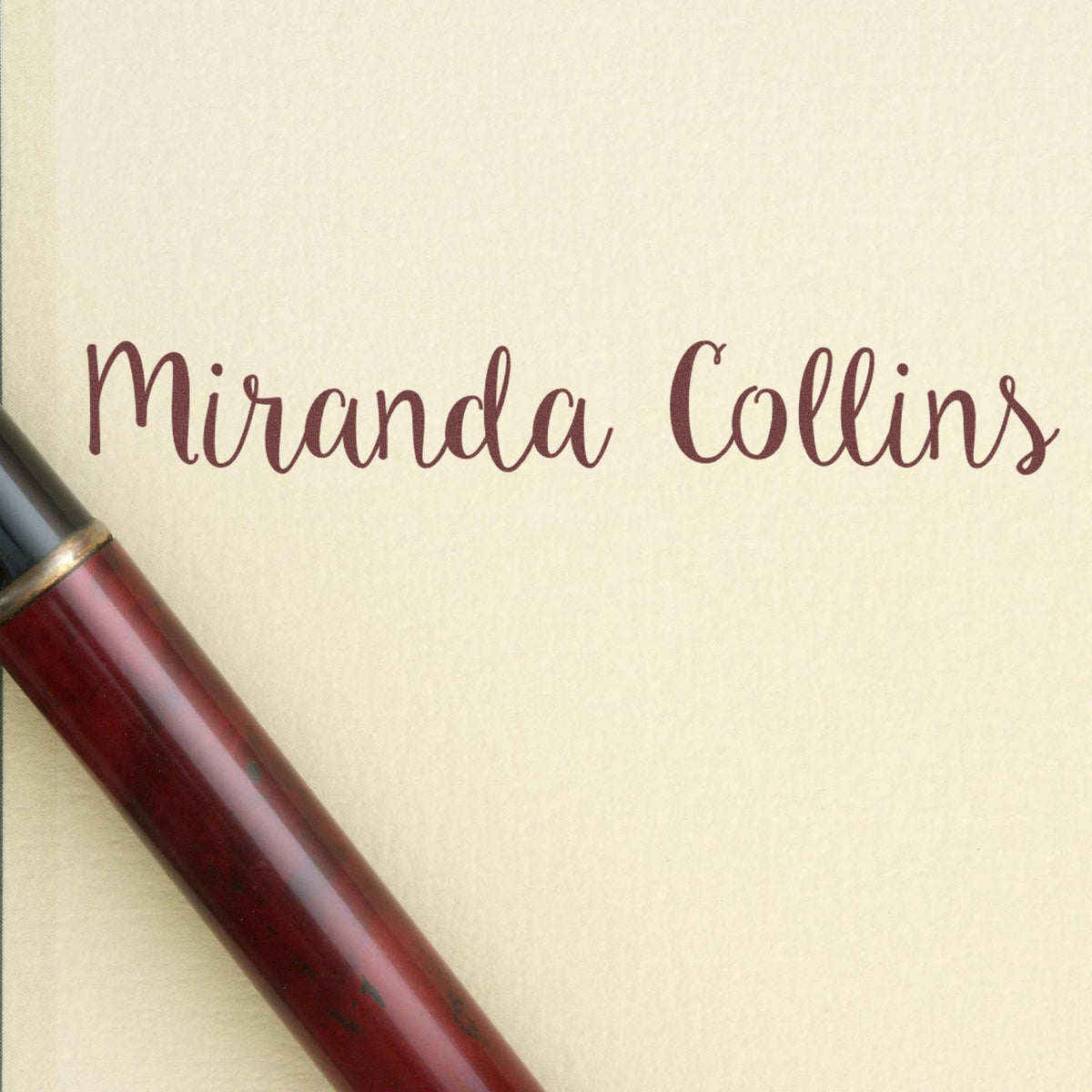 Burgundy custom wax seal stamp with Miranda Collins in elegant script on cream paper, maroon handle visible.