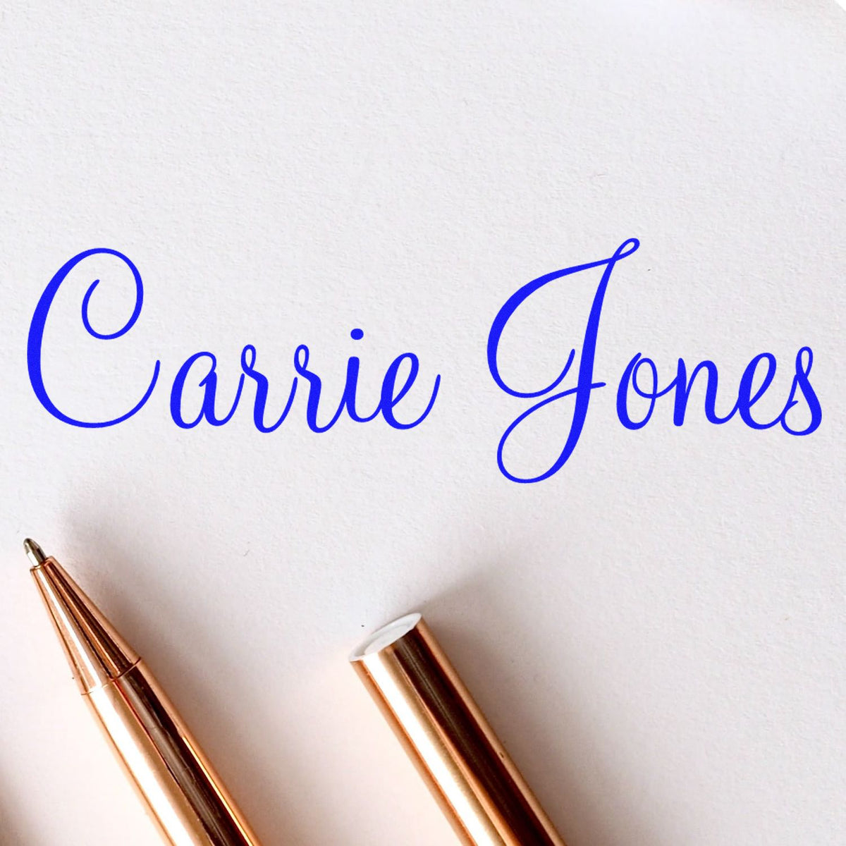Blue Carrie Jones script with rose gold stamp and seal pens on white paper background
