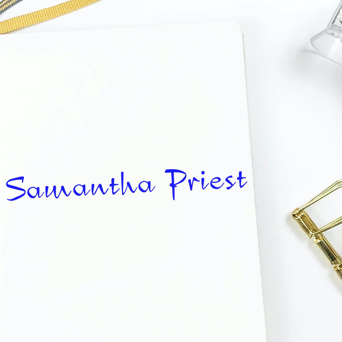 Custom blue name stamp on white paper, with gold seal accents and gold clip.