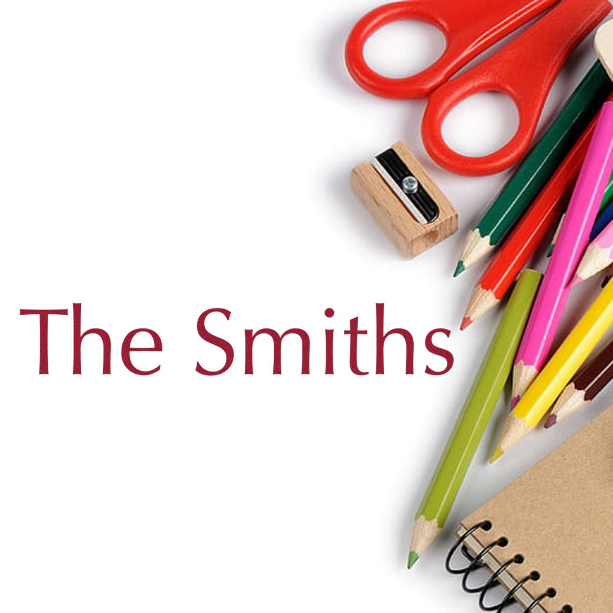 Custom seal stamp with The Smiths text, red scissors, colorful pencils, sharpener, and spiral notebook on white background.