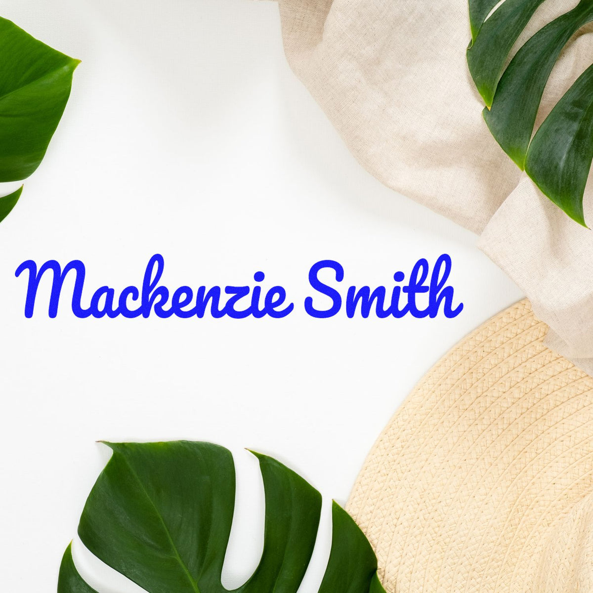 Blue Mackenzie Smith custom stamp and seal on white background with green tropical leaves, beige fabric, and woven hat.