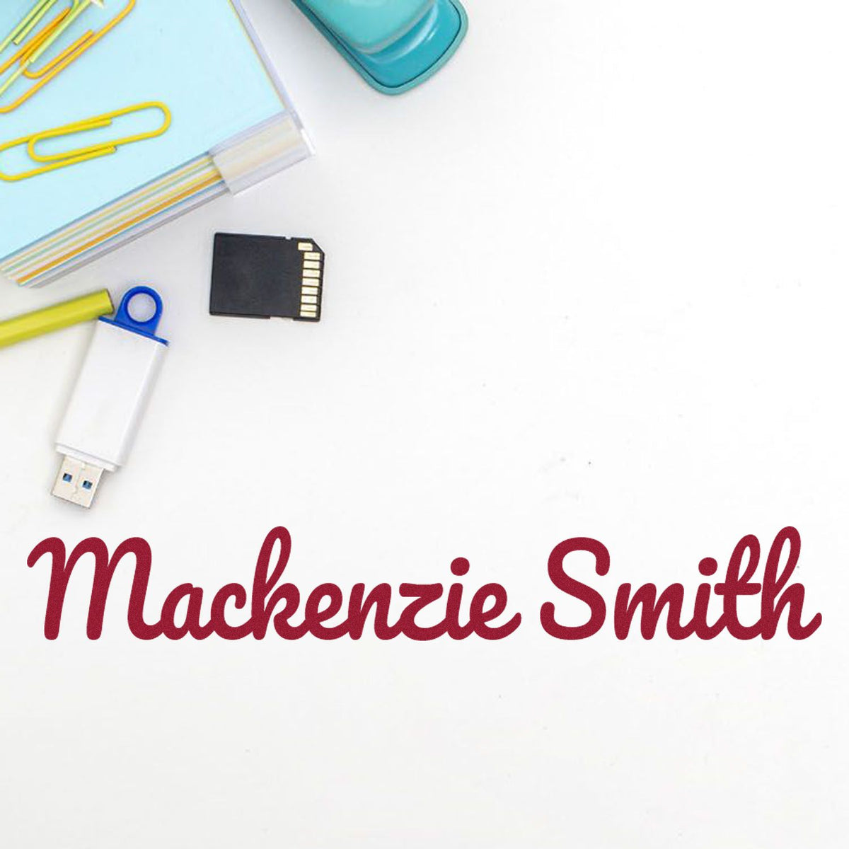 Burgundy custom stamp and seal for Mackenzie Smith with blue stationery, yellow paper clips, USB drive, and SD card.