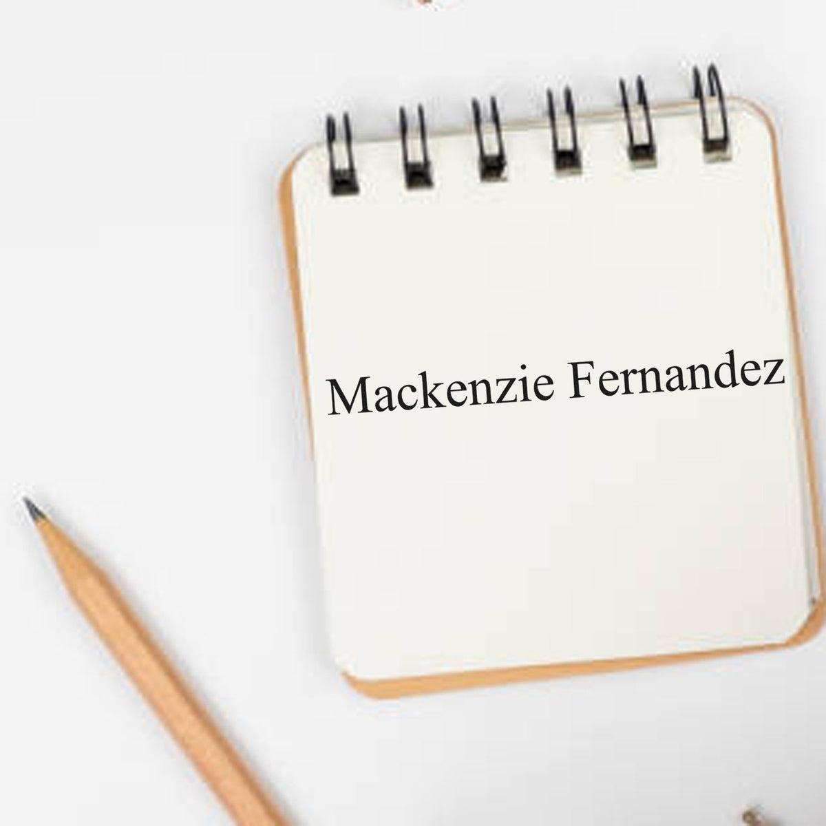 Custom stamp/seal on cream spiral notepad with black Mackenzie Fernandez text and a wooden pencil.