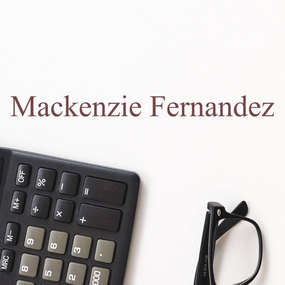 Maroon Mackenzie Fernandez stamp and seal on white paper with black calculator and eyeglasses