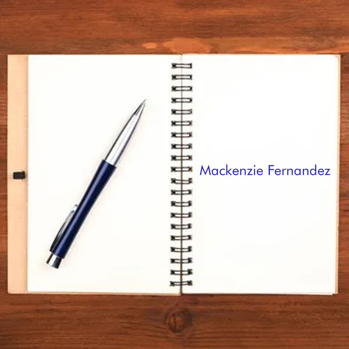 Blue custom stamp and seal with Mackenzie Fernandez on an open spiral notebook beside a navy pen.