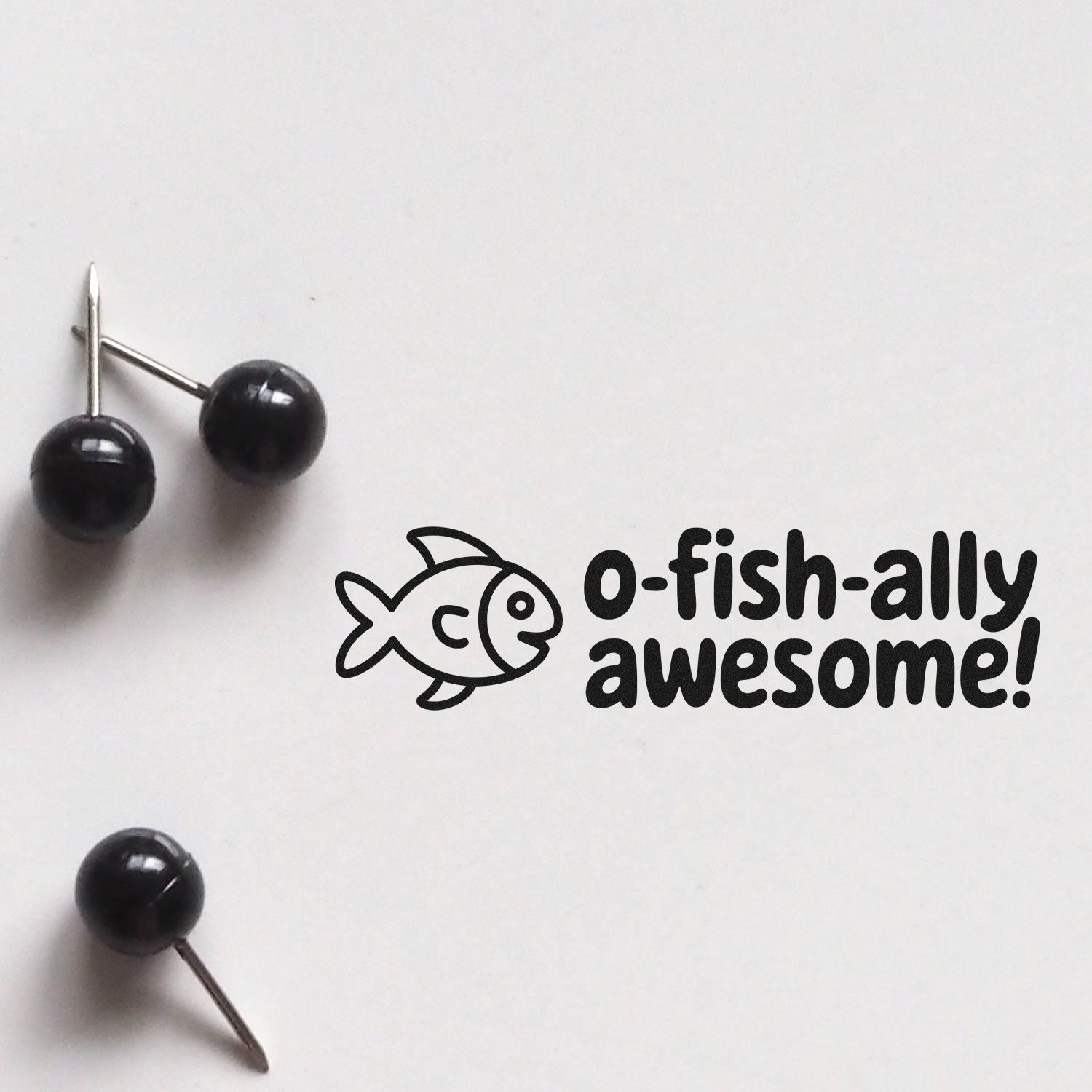Black custom stamp and seal with fish icon and o-fish-ally awesome! text on white background, beside black push pins.