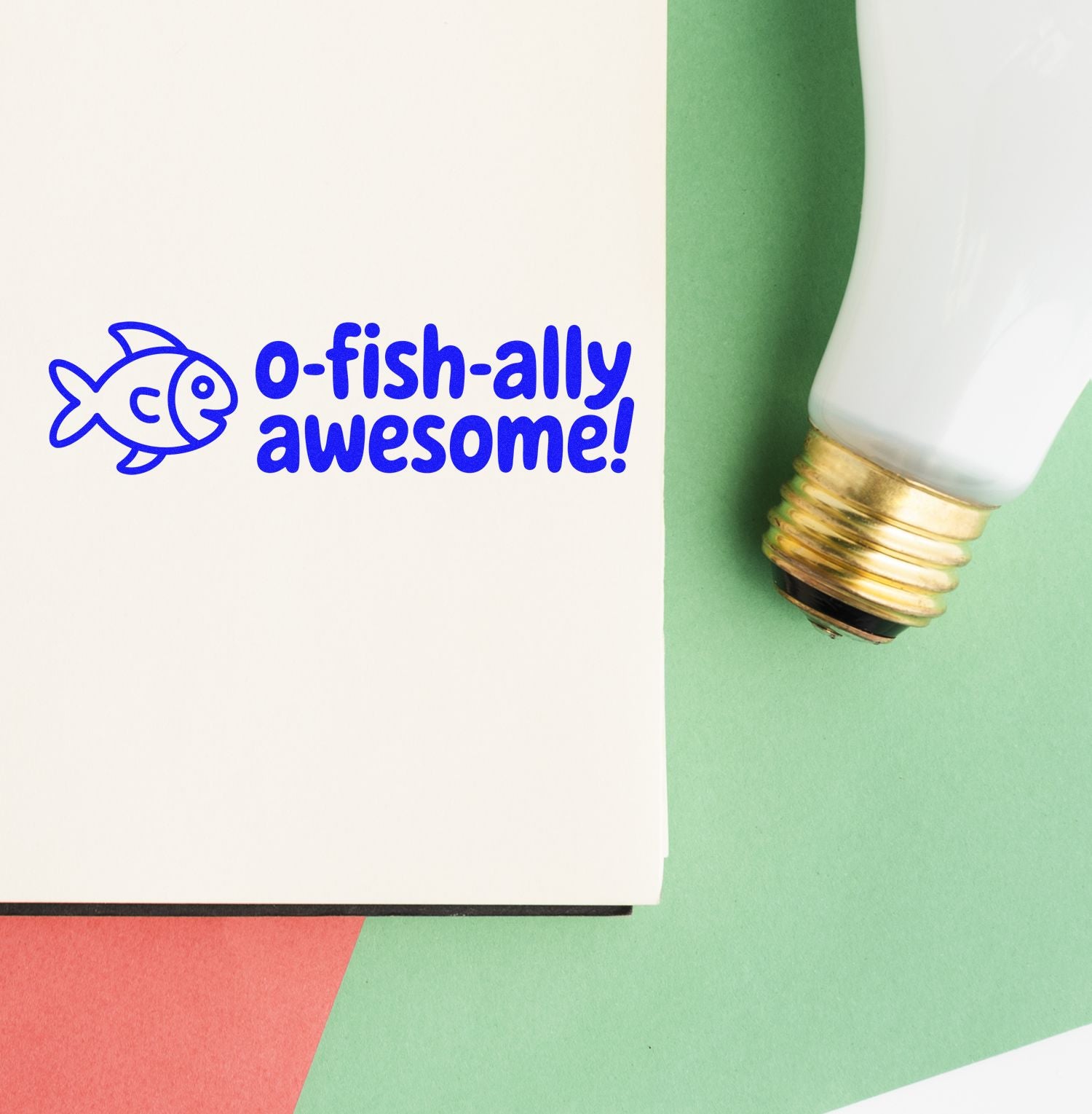 Blue fish stamp reading O-fish-ally awesome! beside a white-and-gold stamp-and-seal applicator on cream and green paper.