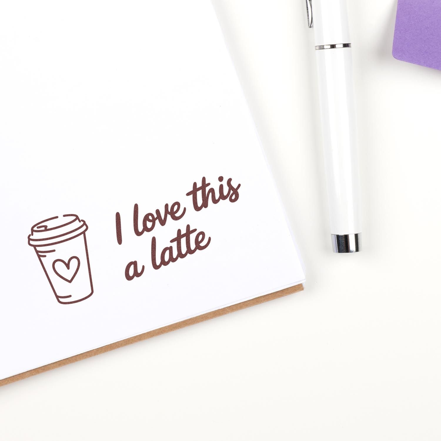 Brown coffee-themed stamp and seal reading I love this a latte with heart cup icon, plus a white pen and purple card.