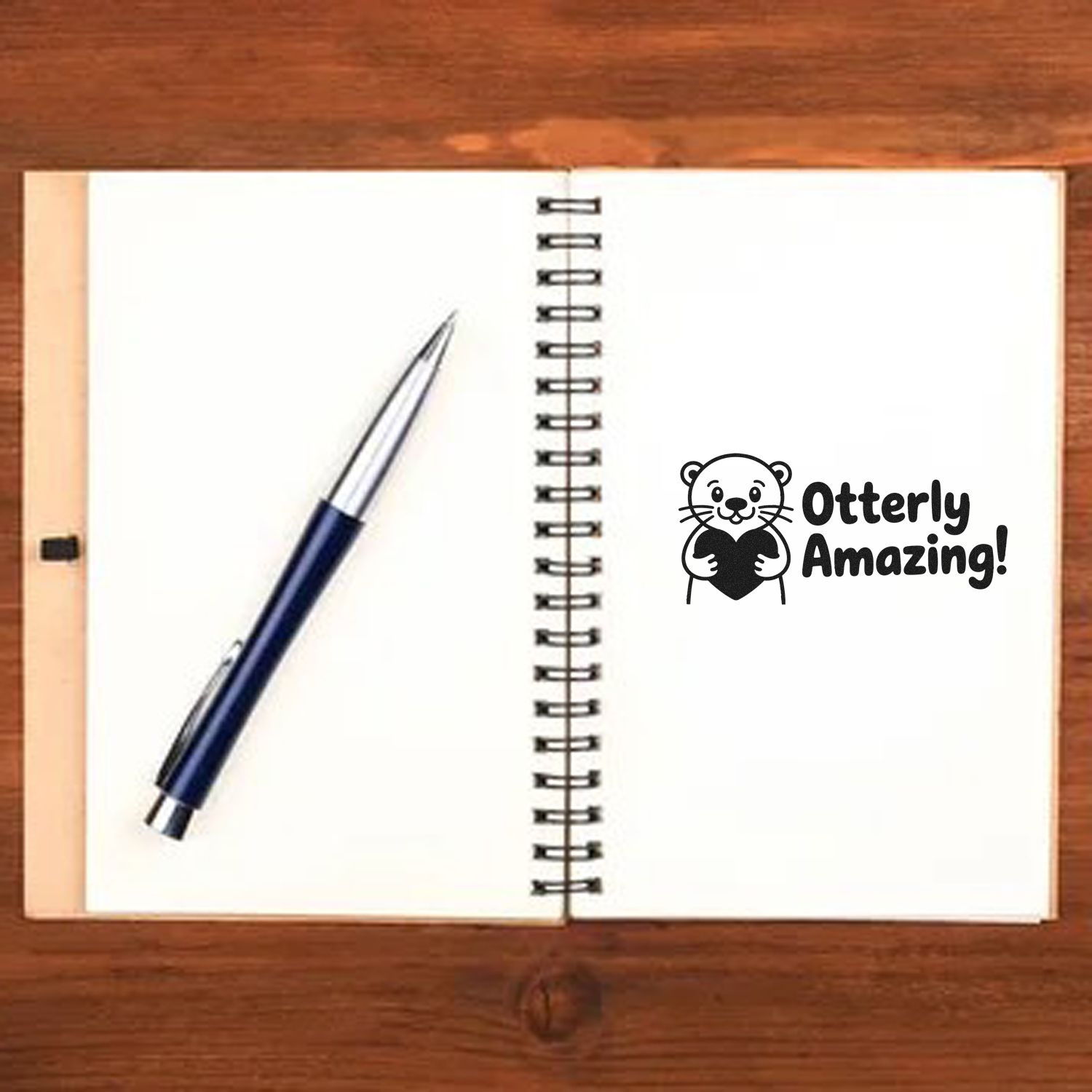 Black otter stamp seal reading Otterly Amazing! beside a navy pen on a spiral notebook.