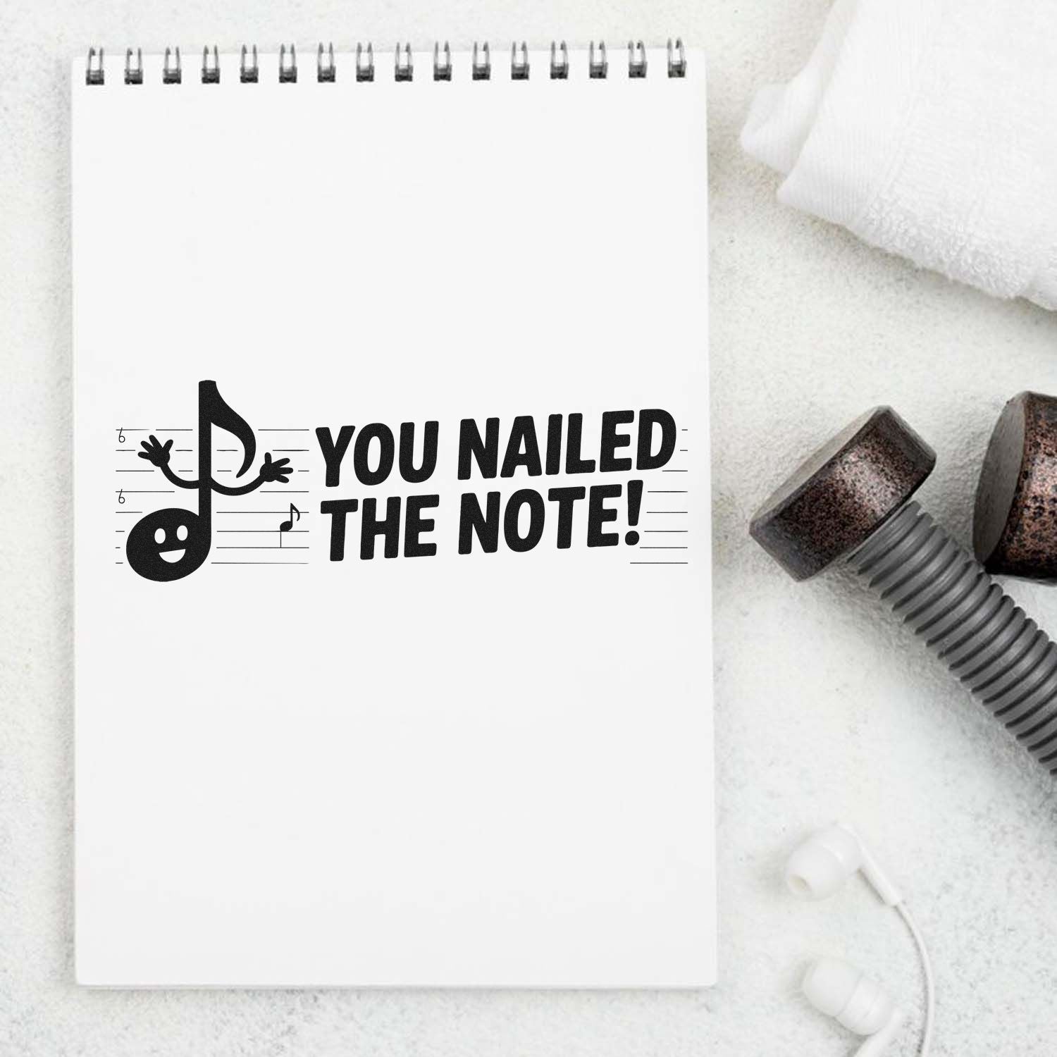 Black stamp and seal on white spiral notebook reading You Nailed the Note! with music note mascot and lined accents.