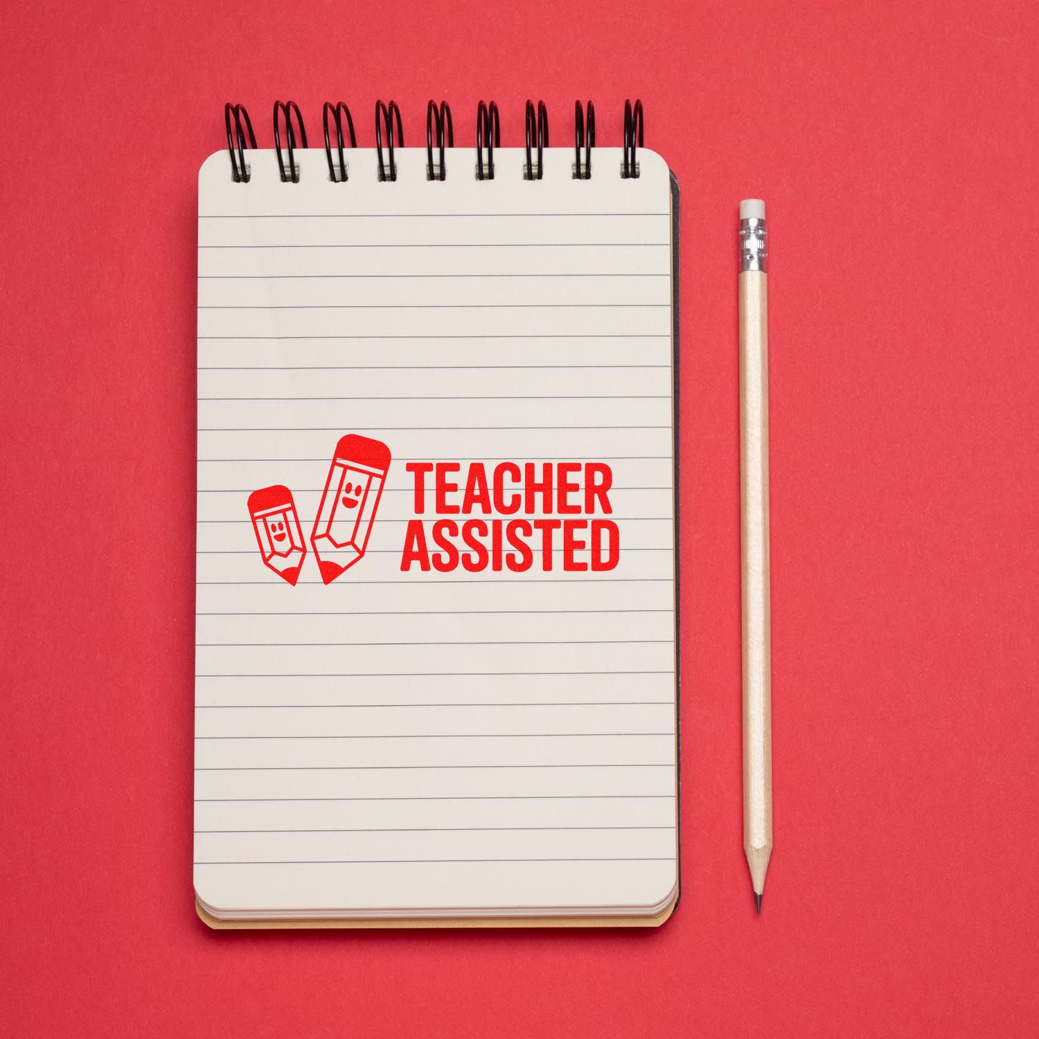 Red Teacher Assisted rubber stamp on a lined notebook beside a pencil on a pink background