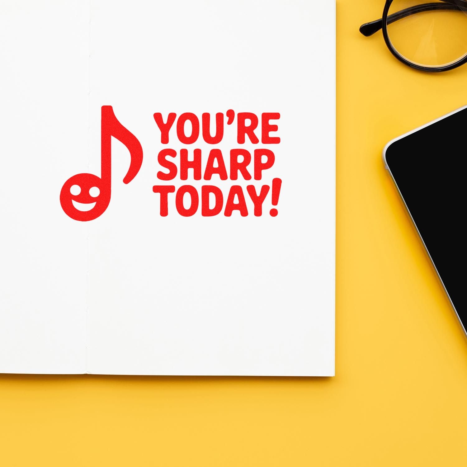 Red stamp seal reading Youre sharp today! on a white page, with yellow background, glasses, and smartphone.