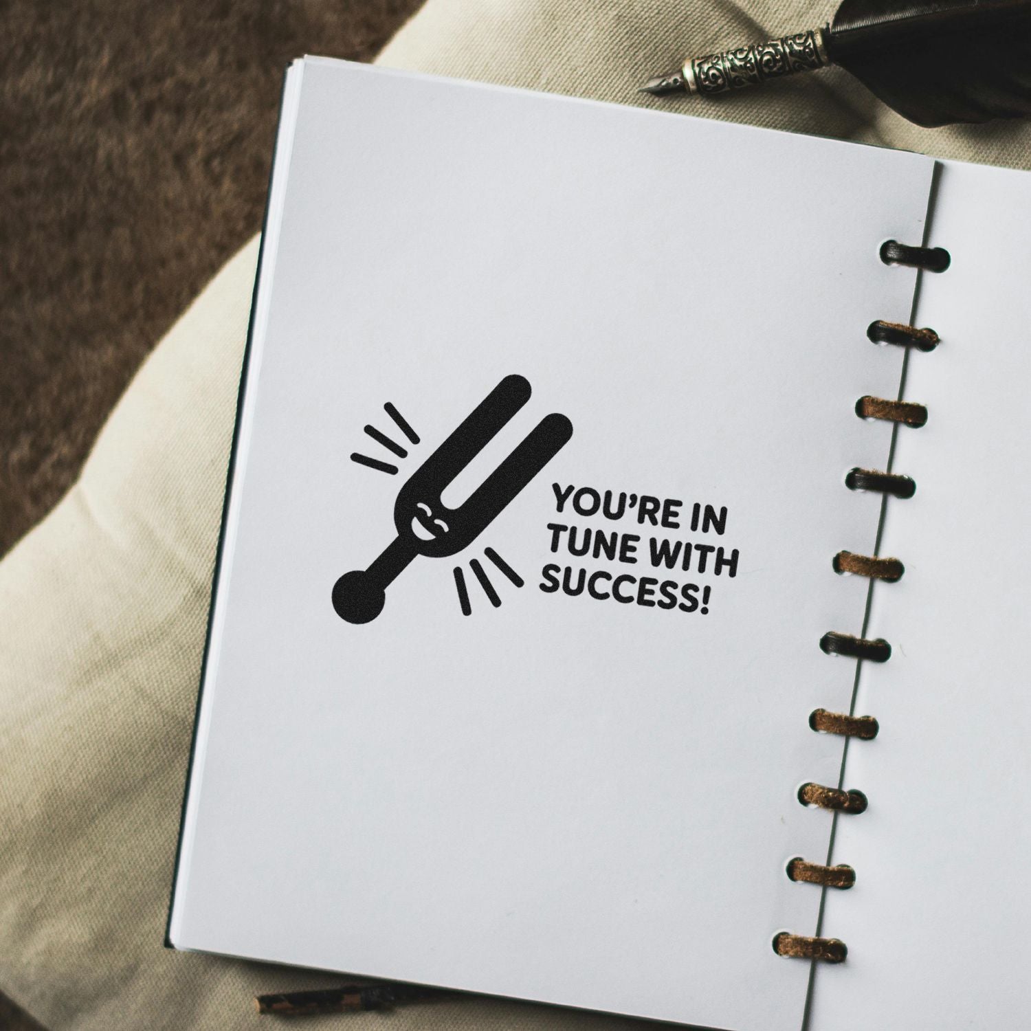 Black motivational stamp seal on a white spiral notebook, with a tuning fork and Youre in tune with success!