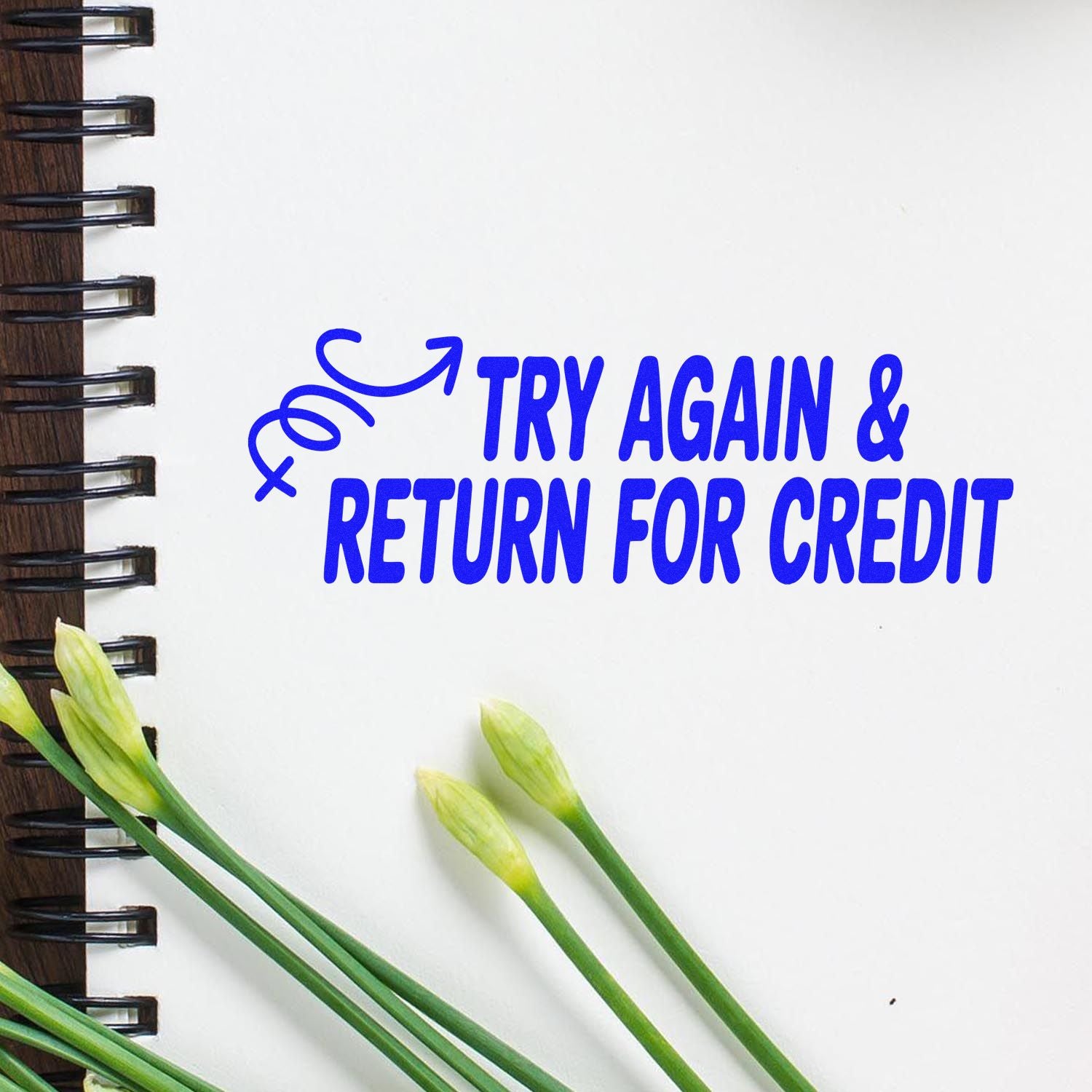 Blue stamp and seal with Try Again & Return for Credit on white page, beside green flower buds and spiral binding.