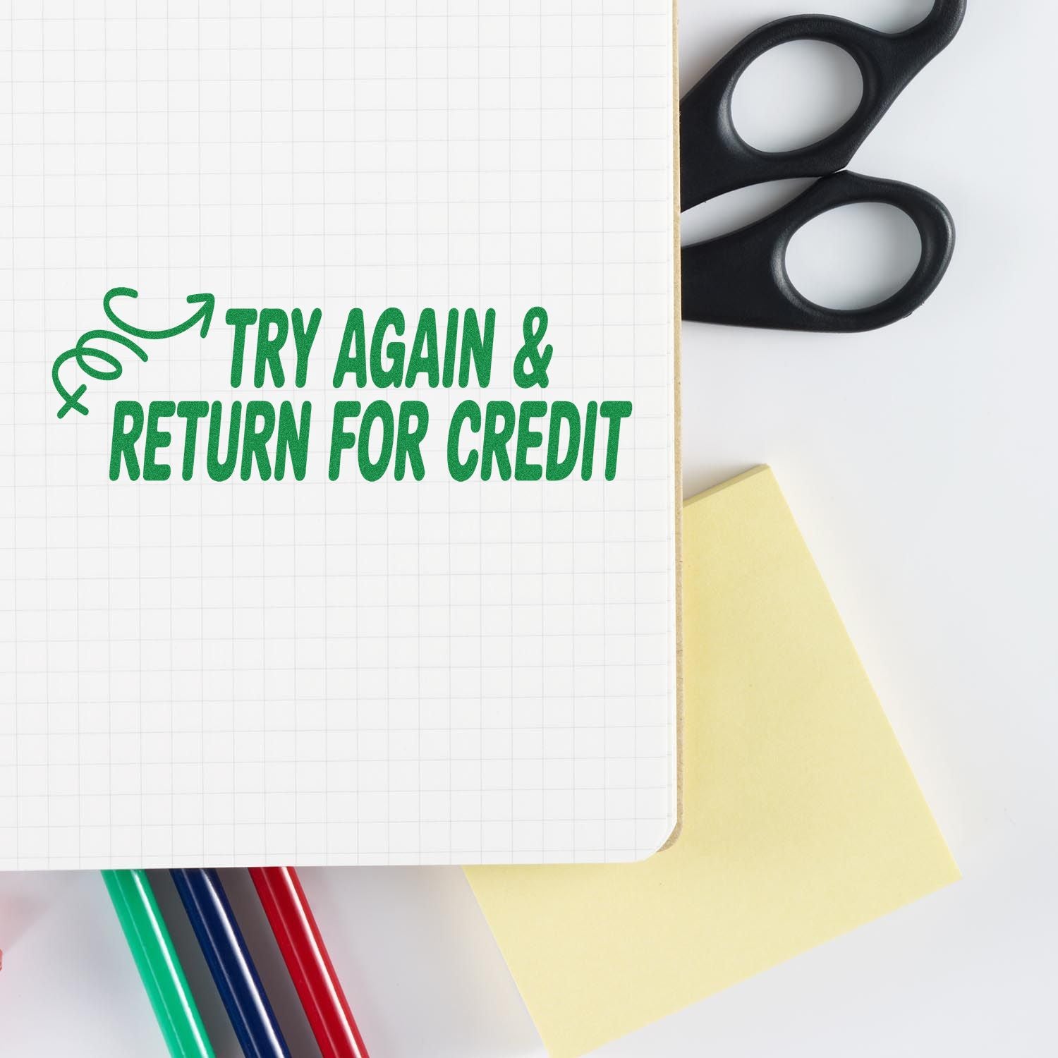 Green try again & return for credit stamp on graph paper, with black scissors, yellow note, and colored pens.
