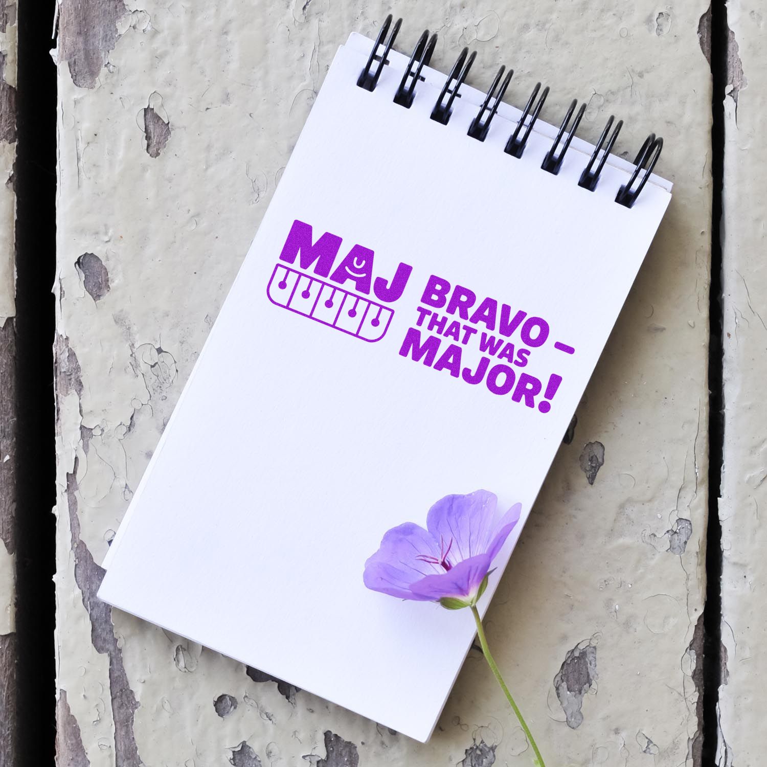 White spiral notebook featuring a purple custom stamp and seal reading MAJ BRAVO  THAT WAS MAJOR! with lavender flower.