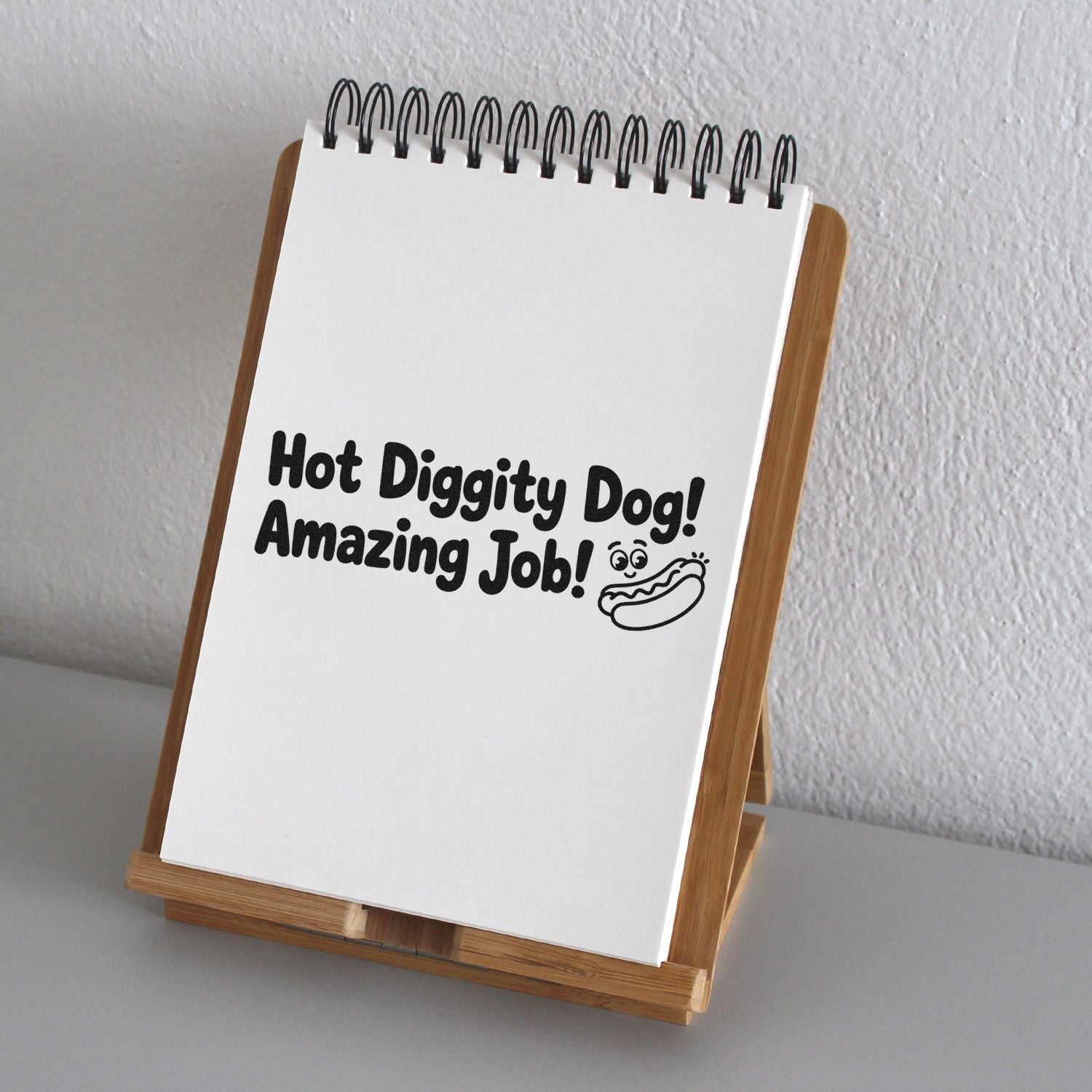 Black hot dog praise rubber stamp on a white spiral notepad in a wooden display stand