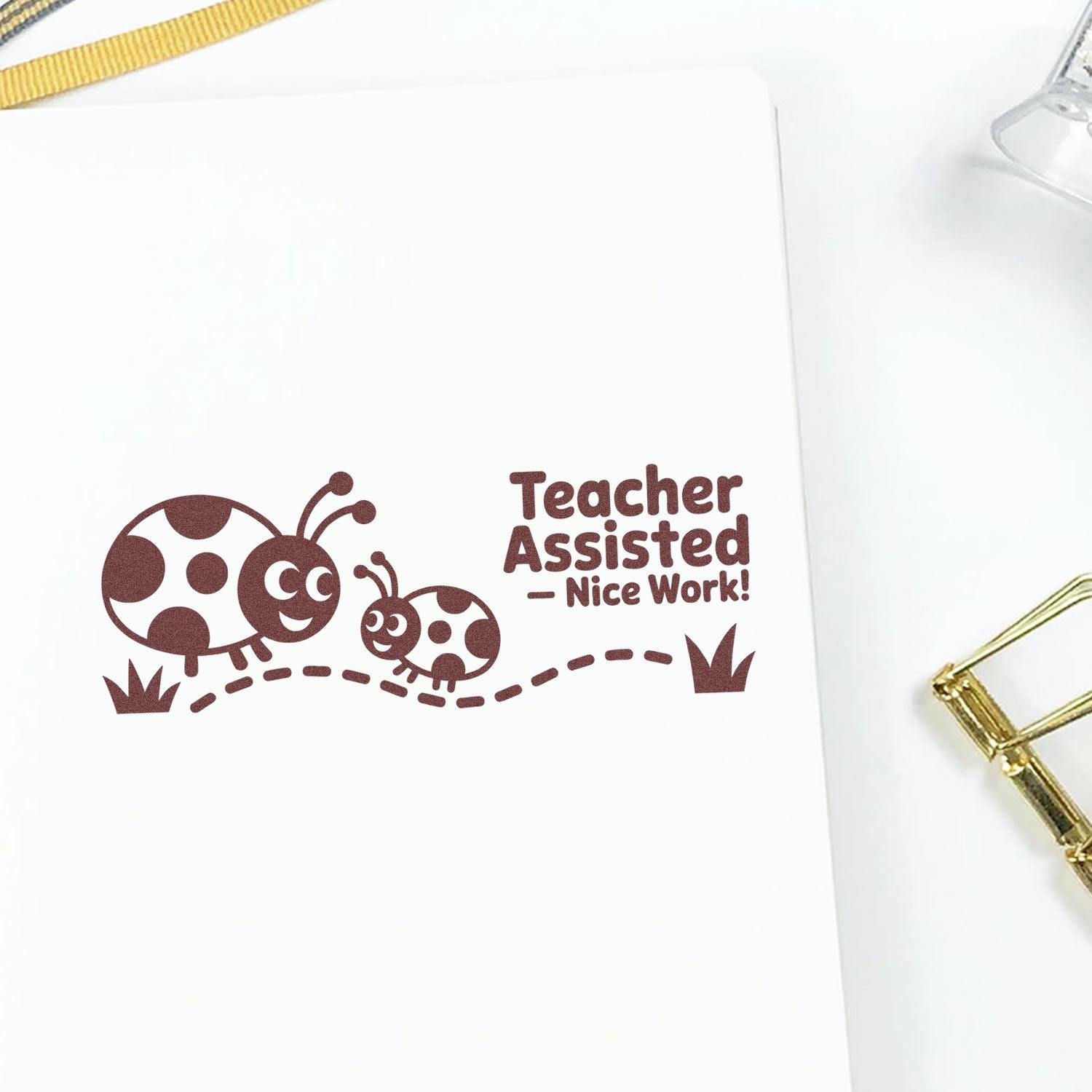Brown teacher stamp reading Teacher Assisted  Nice Work! with two ladybugs and dotted path on white paper.