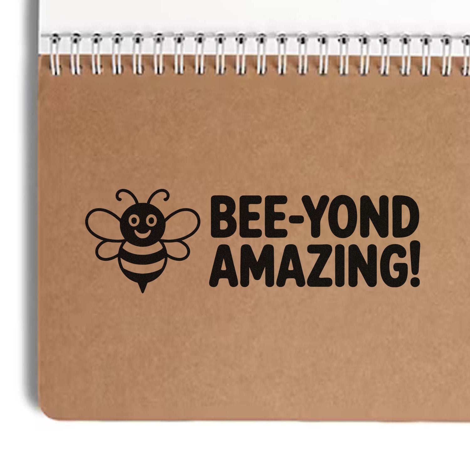Black bee stamp seal with BEE-YOND AMAZING! on kraft brown spiral notebook cover, black lettering and bee graphic