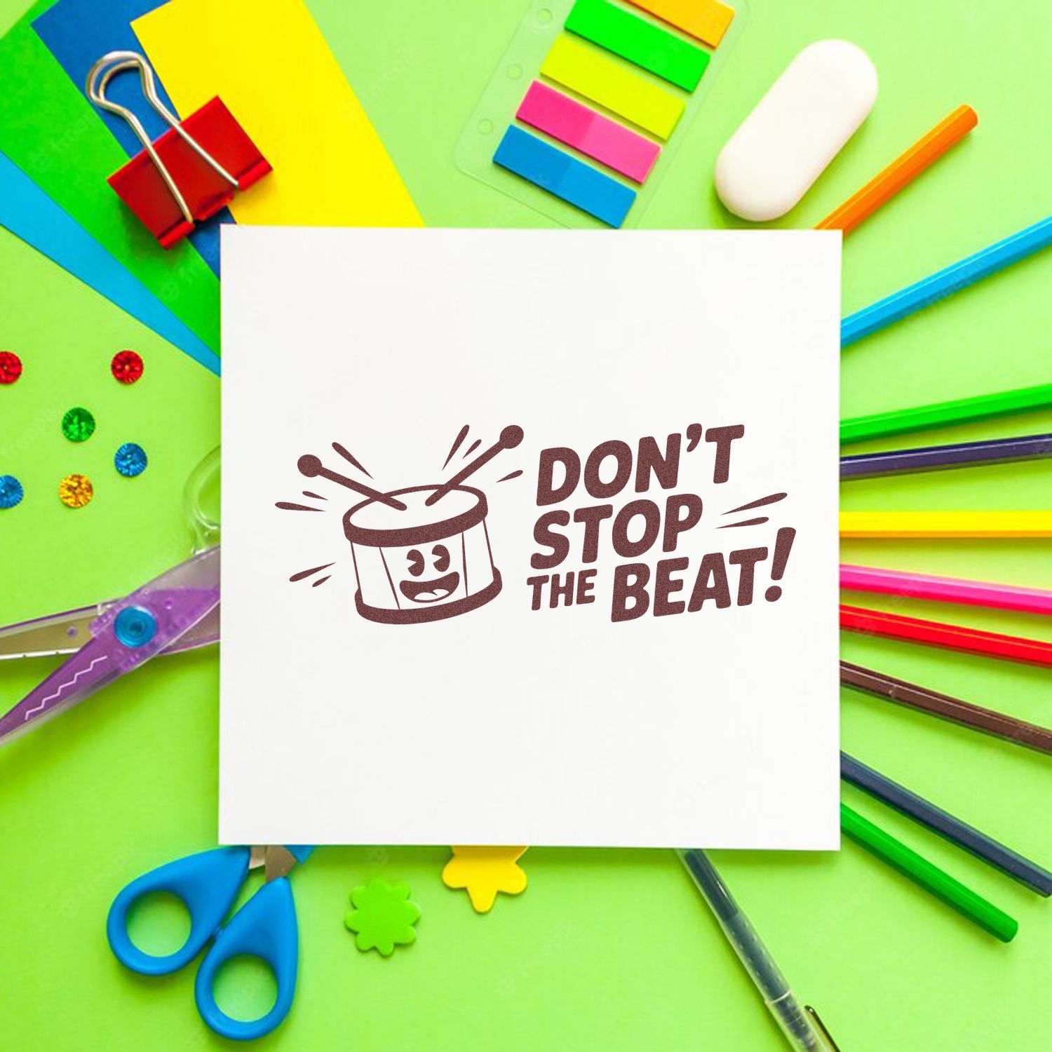 White card with maroon drum stamp seal reading DONT STOP THE BEAT! surrounded by colorful stationery on a green background.