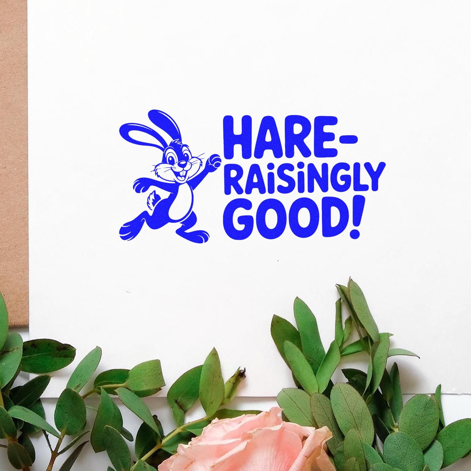 Blue rabbit stamp/seal with HARE-RAISINGLY GOOD! on white paper, framed by green leaves and a pink rose.