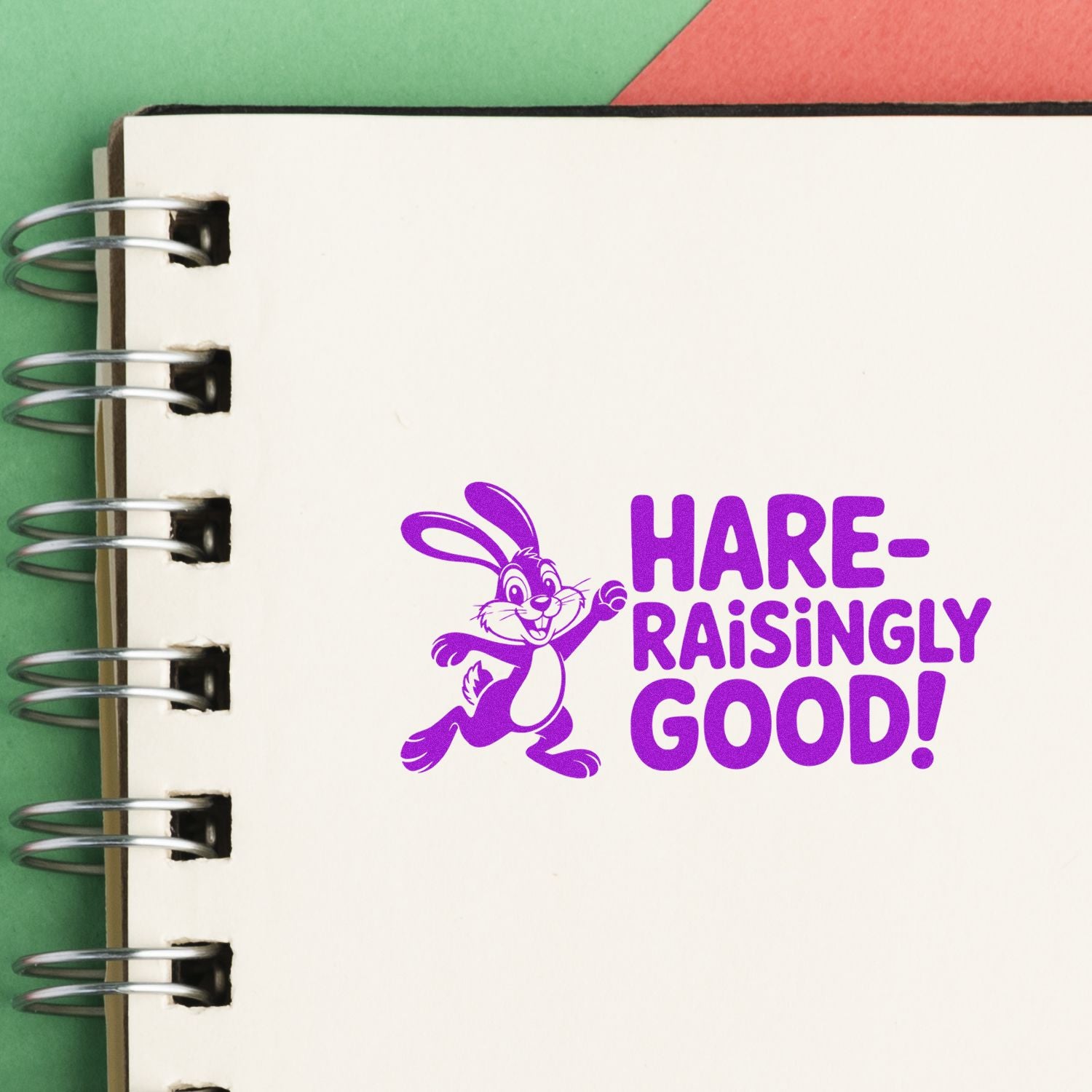 Purple rabbit stamp seal with Hare-raisingly Good! on a white spiral notebook over green and red background.