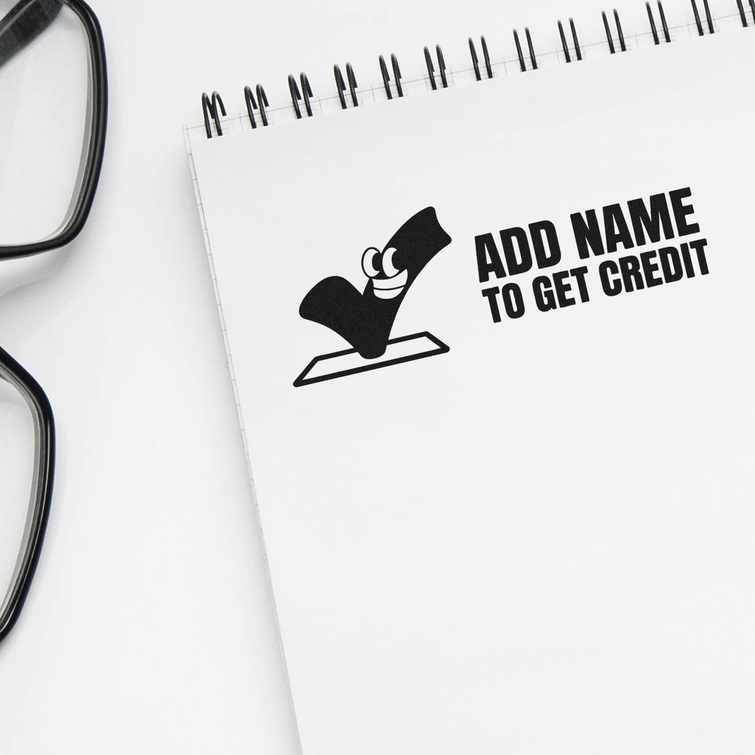 Black custom stamp and seal imprint on white spiral notebook reading ADD NAME TO GET CREDIT.