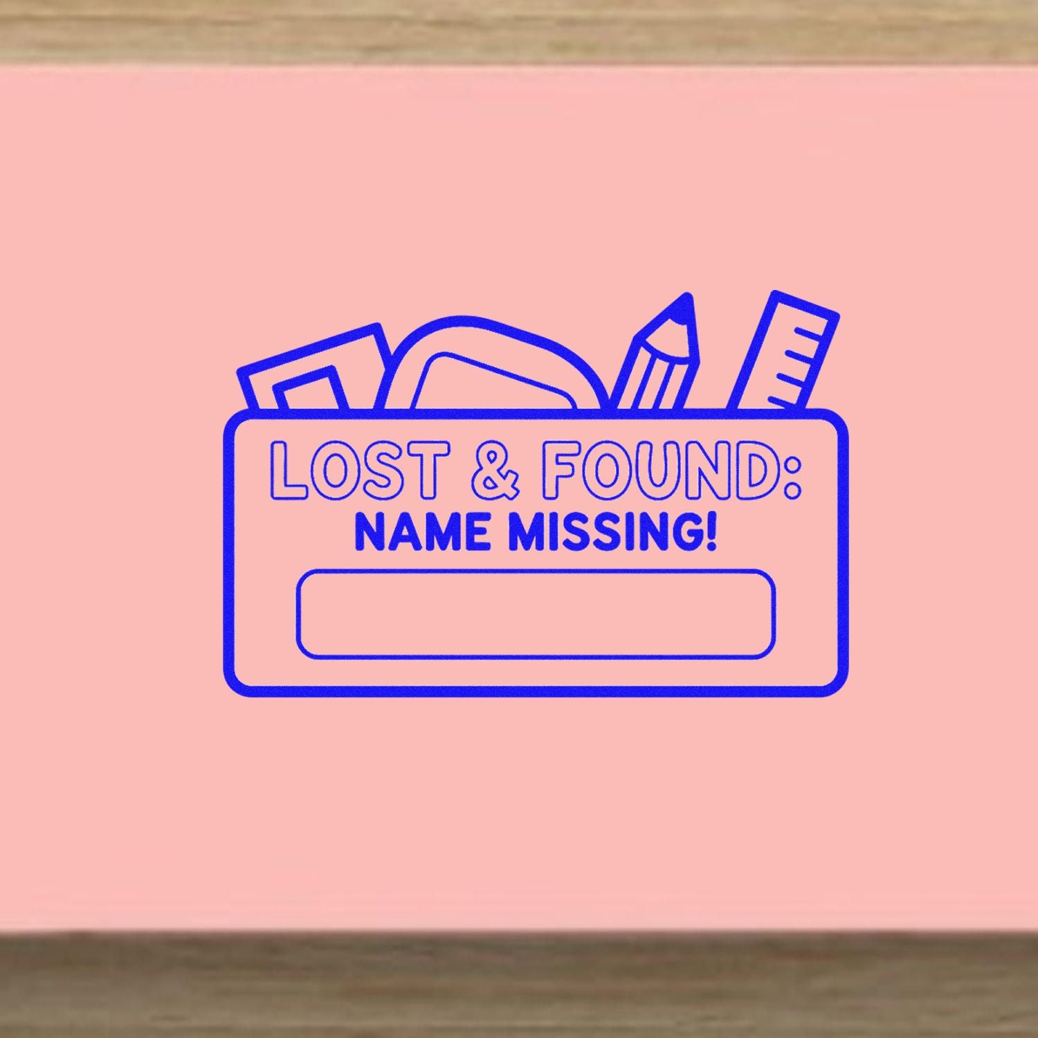 Pink lost-and-found name stamp with blue outline, school supplies, and blank label for custom seal.