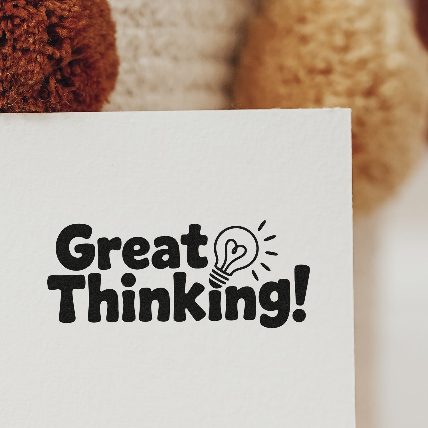Custom black stamp seal reading Great Thinking! with lightbulb icon on white paper, warm brown blurred background.