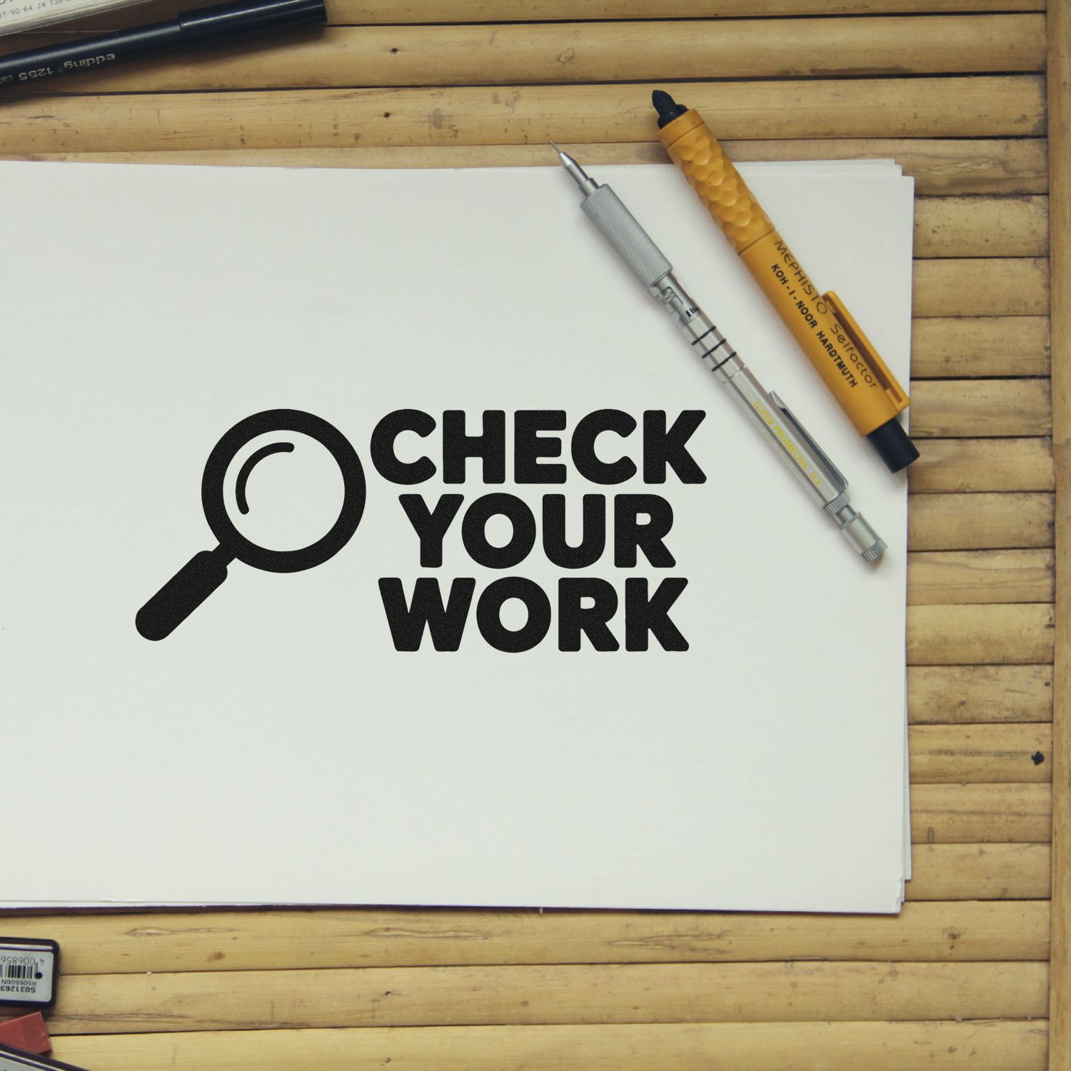 Black stamp and seal design reading Check Your Work with magnifying glass on white paper, beside silver and yellow pens.