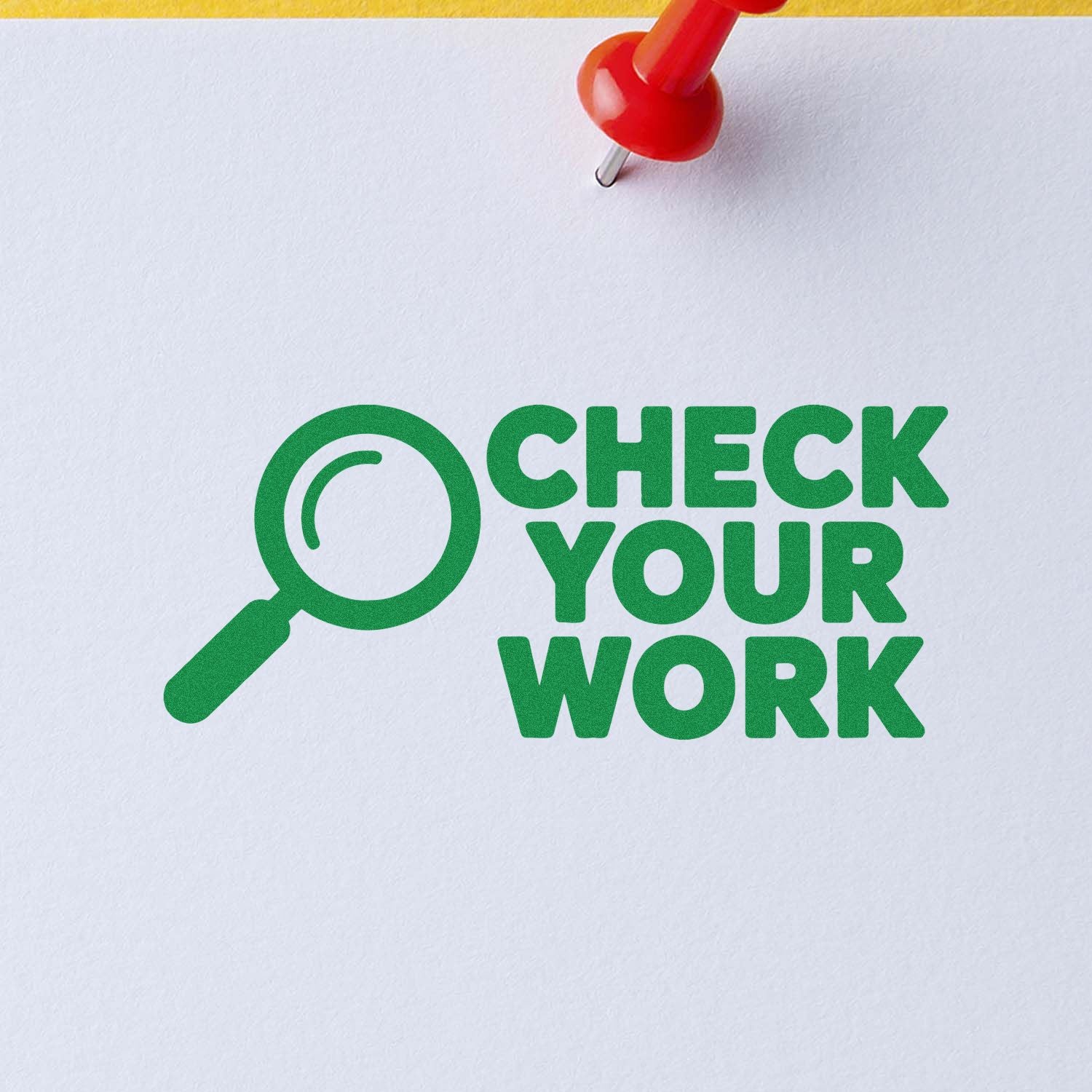 Green check-your-work stamp seal with magnifying glass icon on white paper, secured by a red pushpin.