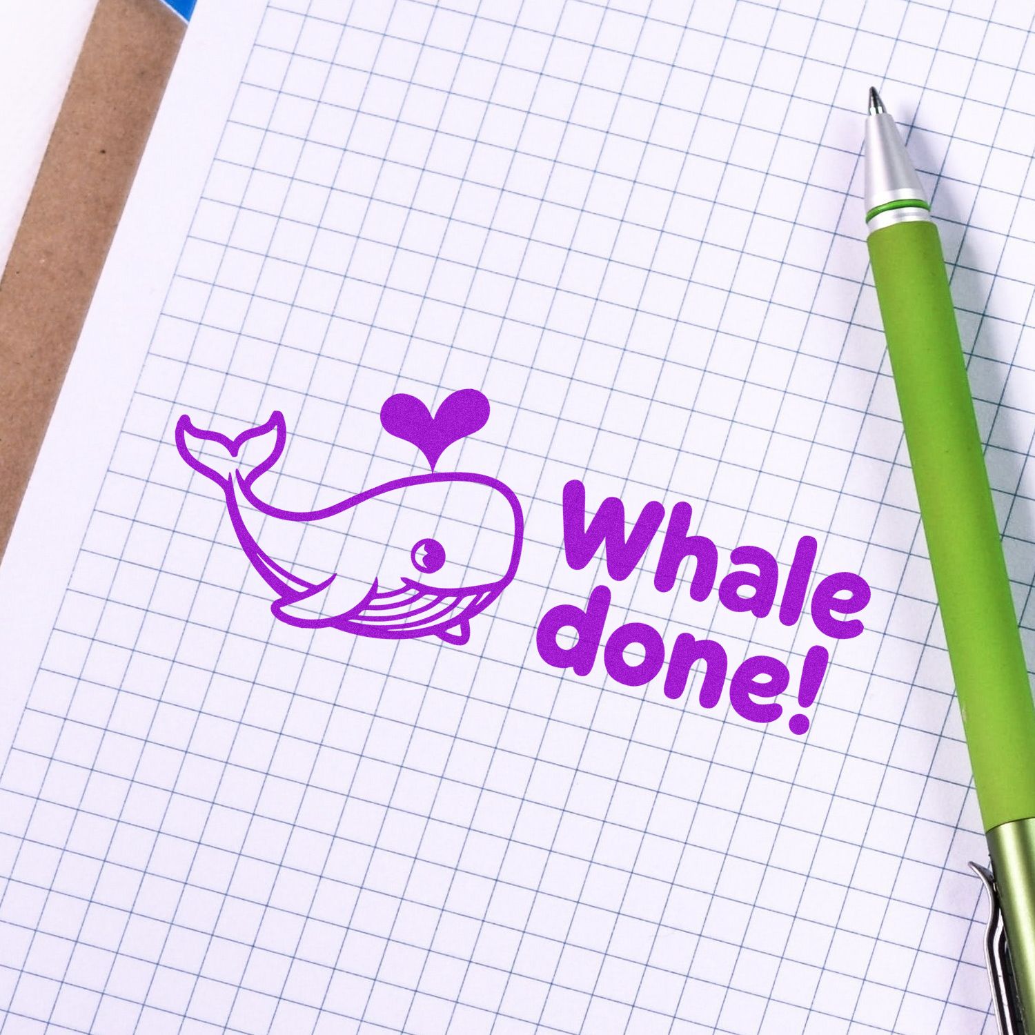 Purple whale custom stamp seal with heart and Whale done! text on graph paper beside a green pen.