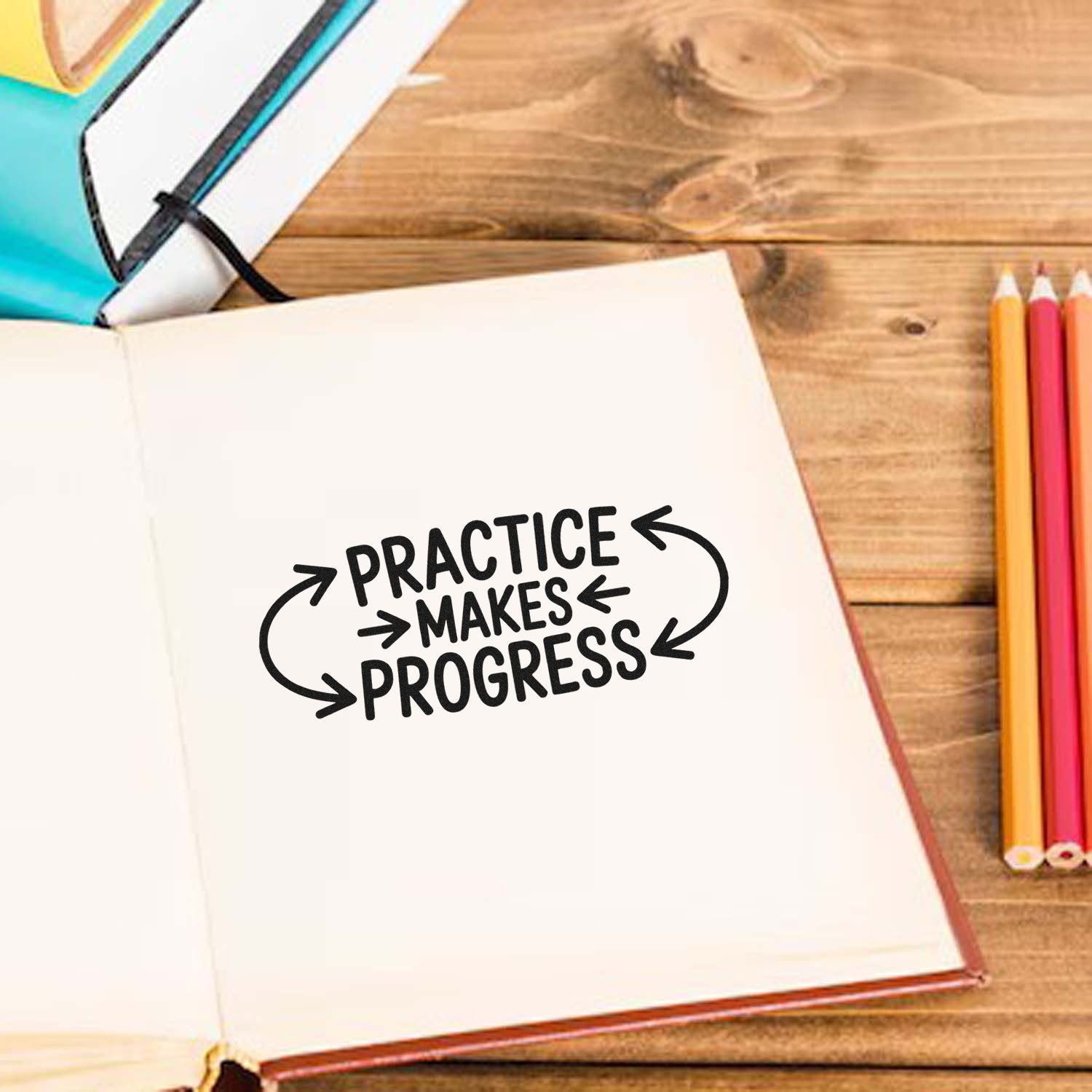 Black motivational stamp seal reading Practice makes progress in an open notebook, with colored pencils on a wooden desk.