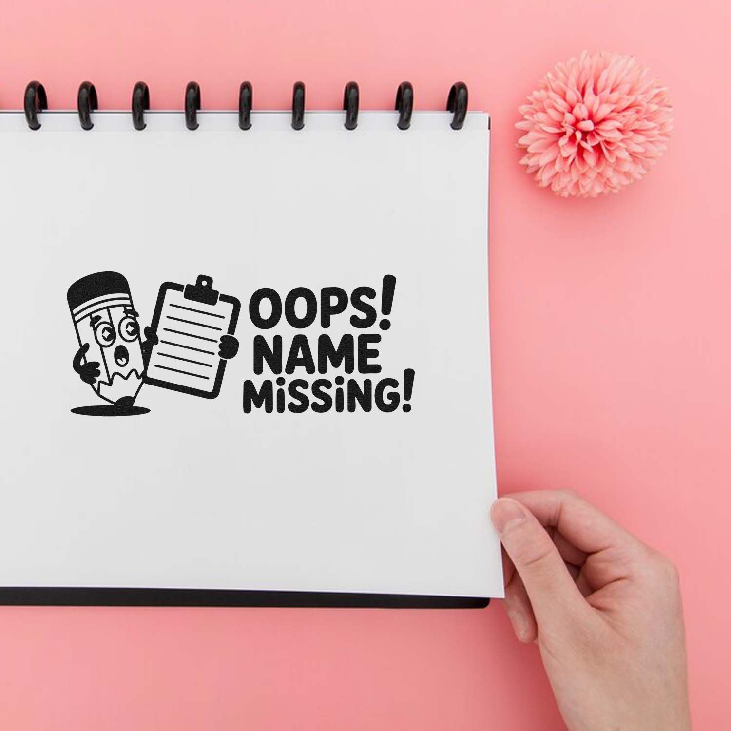 Black Oops! Name Missing stamp design on a white spiral notebook, with clipboard and pencil graphic on a pink background.