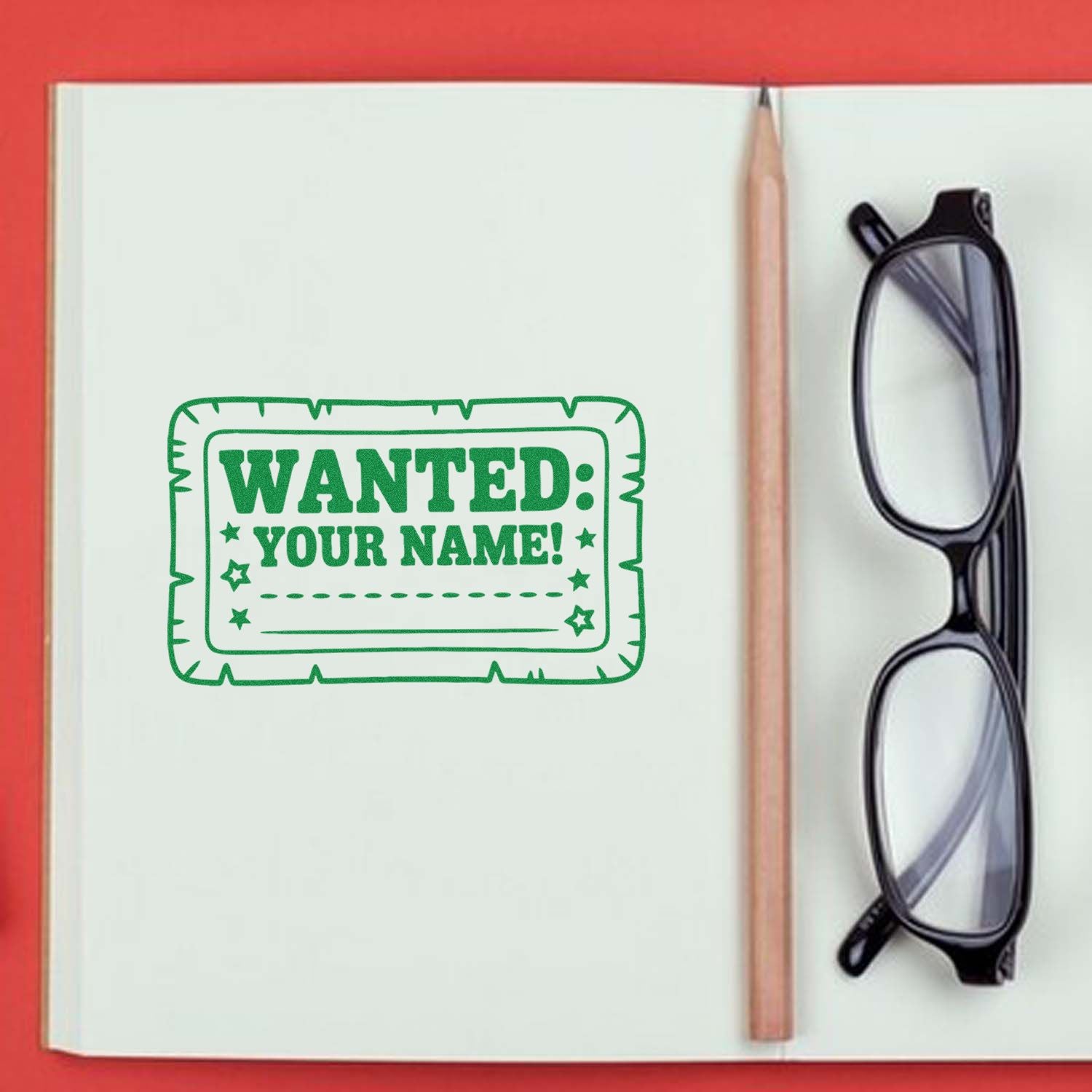 Green custom wanted-name stamp seal on notebook page beside a pencil and black glasses, with red background