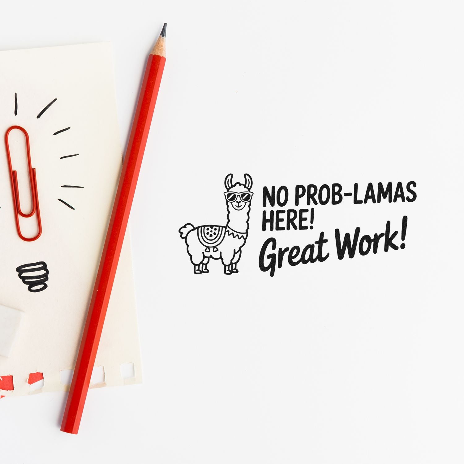 Black llama stamp reading No Prob-Lamas Here! Great Work! beside a red pencil and paperclip on white paper.